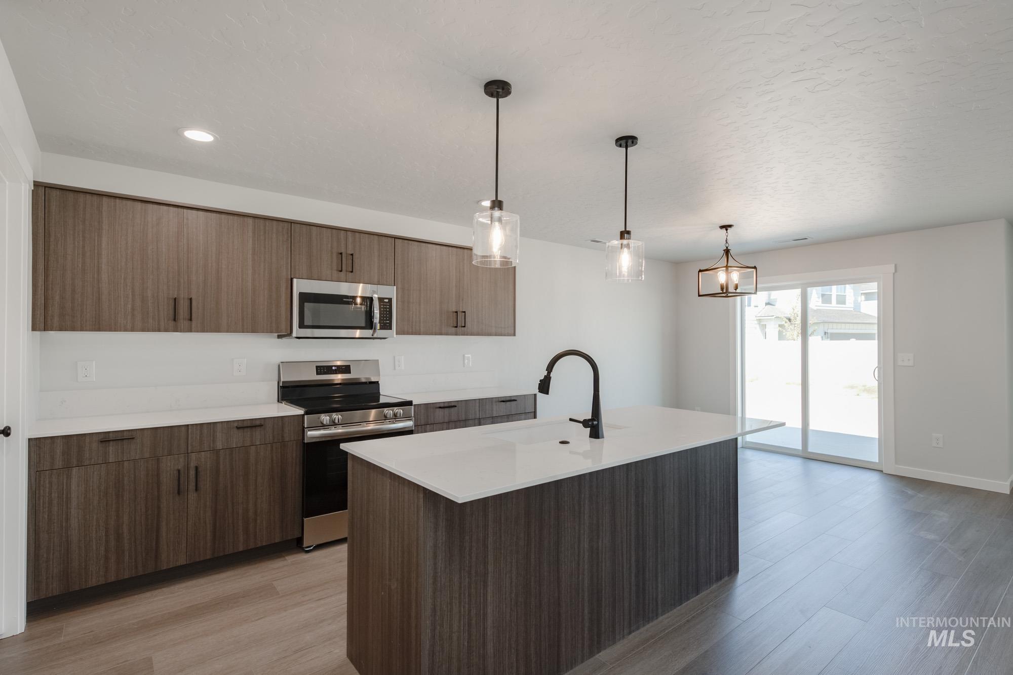 Kitchen with stainless steel appliances, light wood-style floors, pendant lighting, a kitchen island with sink, and recessed lighting