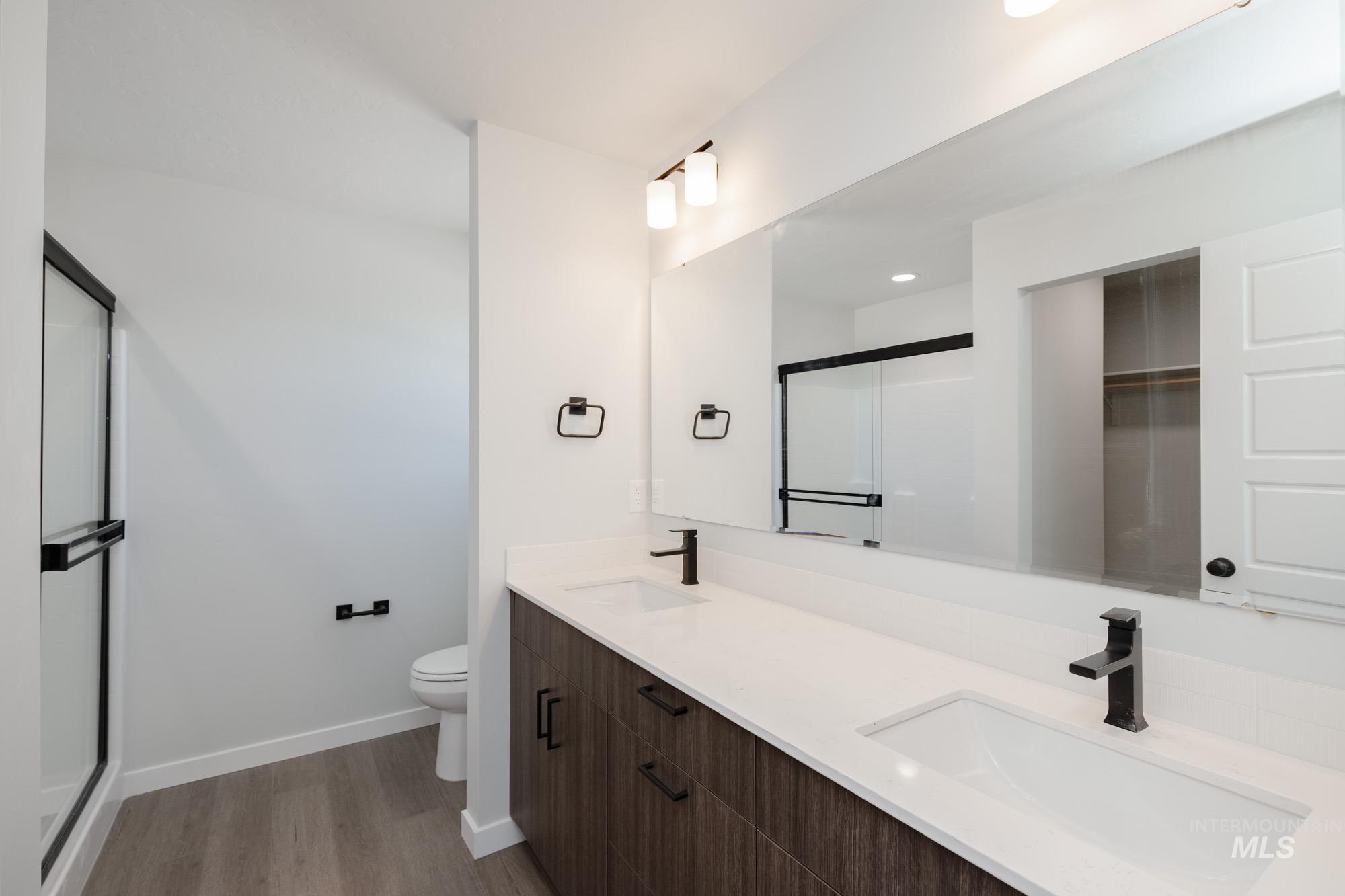 Full bathroom with a shower stall, double vanity, light wood finished floors, recessed lighting, and a spacious closet