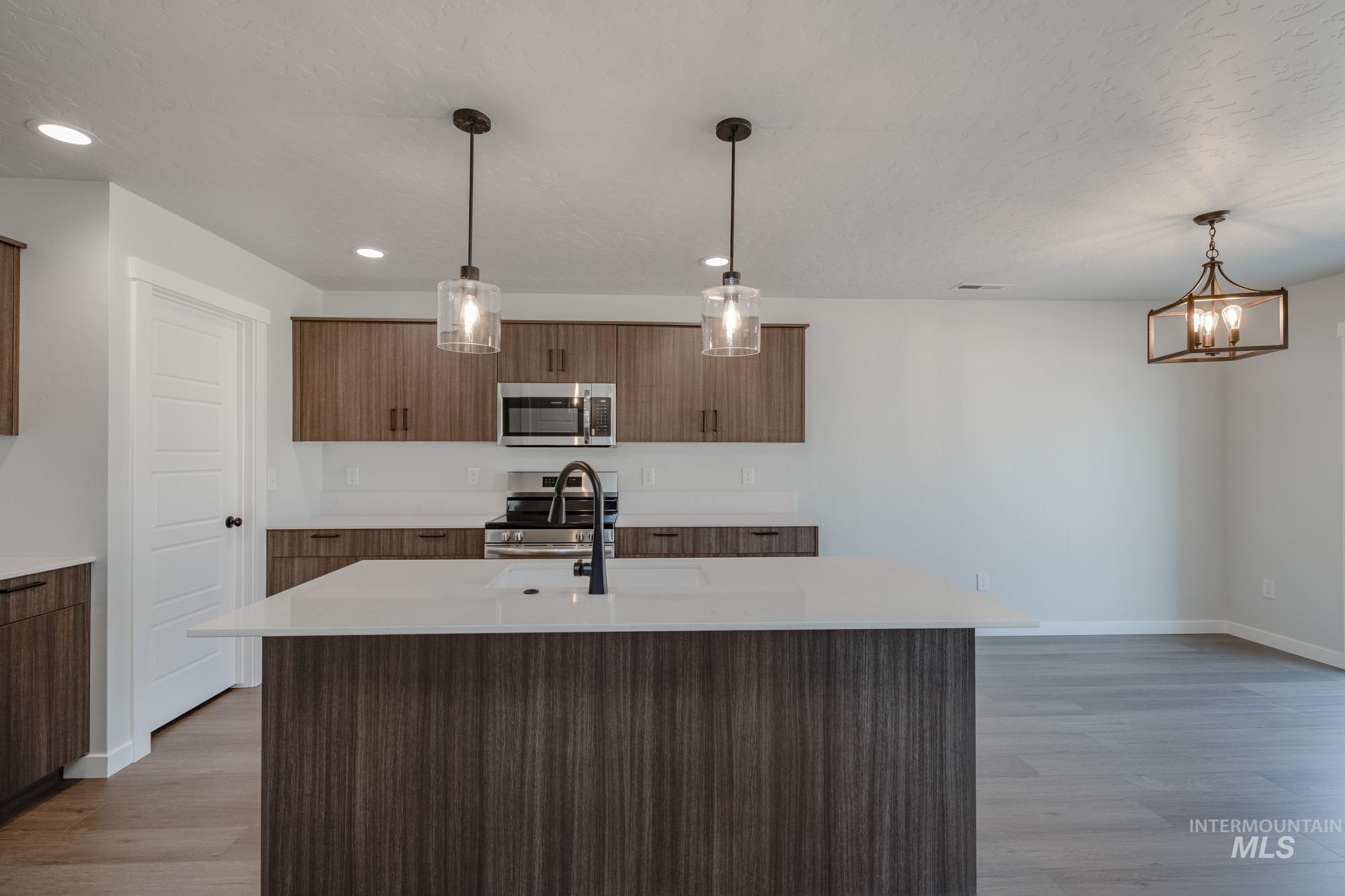 Kitchen with a kitchen island with sink, pendant lighting, appliances with stainless steel finishes, light wood finished floors, and light stone countertops