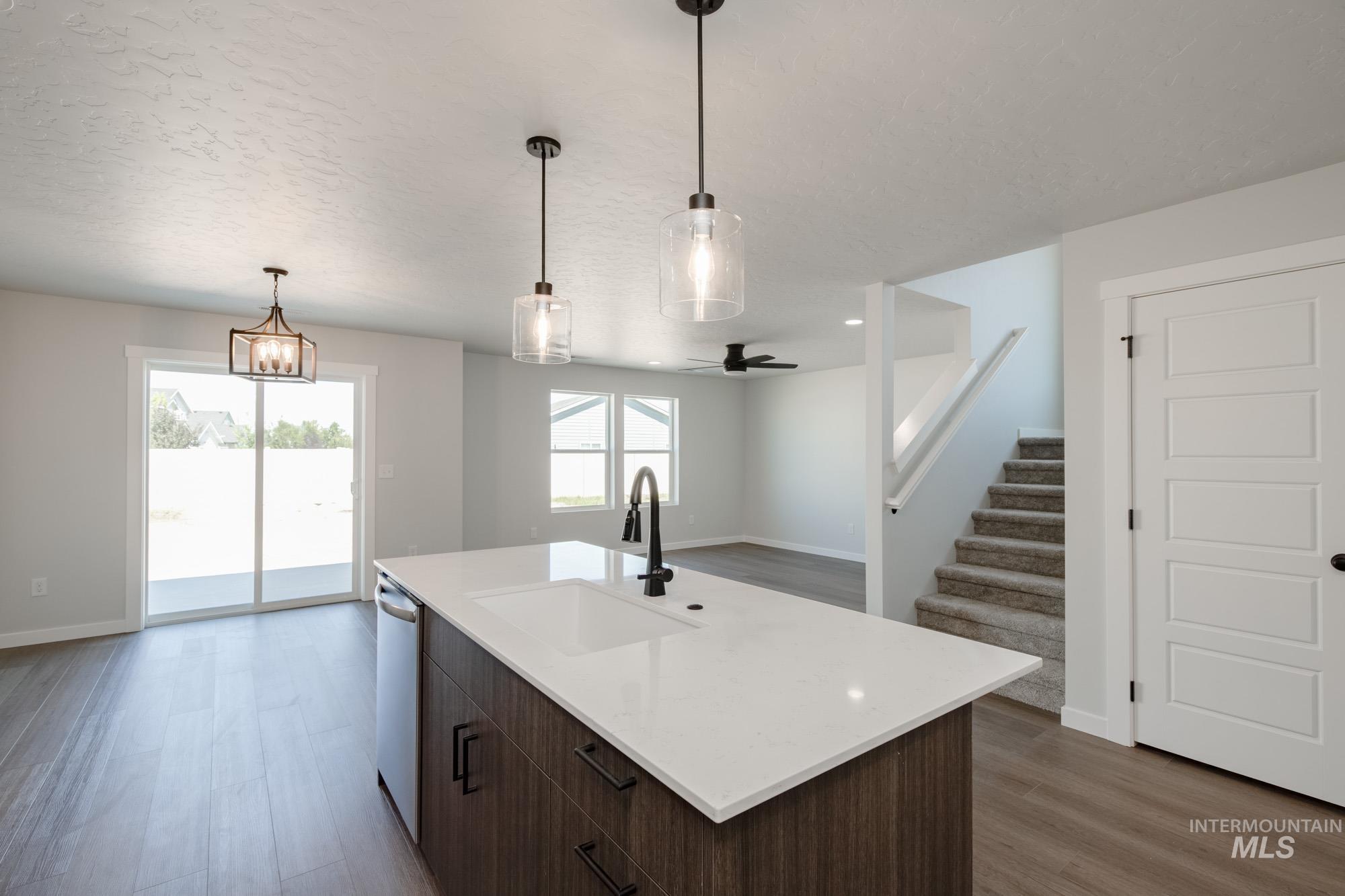 Kitchen featuring dark brown cabinetry, light wood-type flooring, open floor plan, pendant lighting, and a textured ceiling