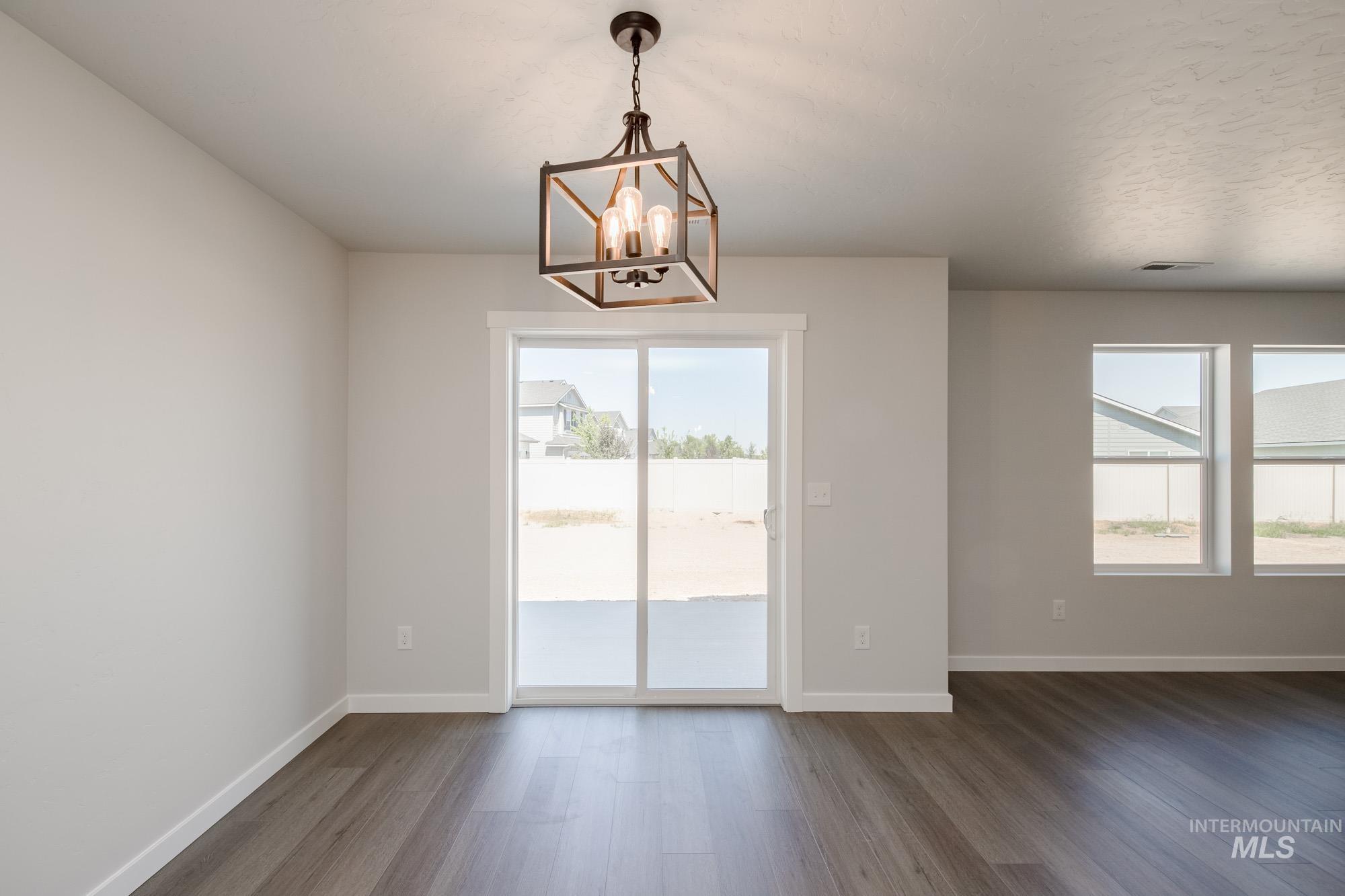 Unfurnished dining area featuring dark wood-style flooring, healthy amount of natural light, and a chandelier
