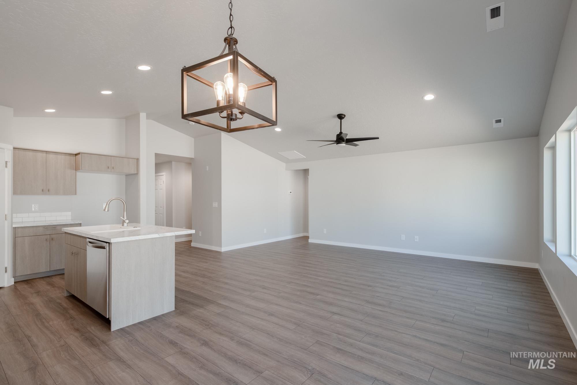 Kitchen with lofted ceiling, an island with sink, decorative light fixtures, light wood-style floors, and a chandelier