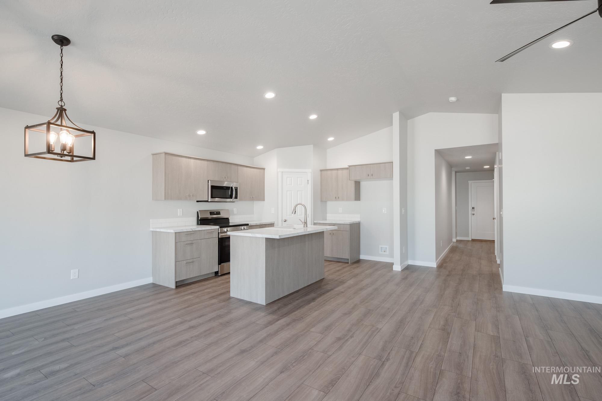 Kitchen featuring open floor plan, lofted ceiling, a kitchen island with sink, light wood-style flooring, and appliances with stainless steel finishes