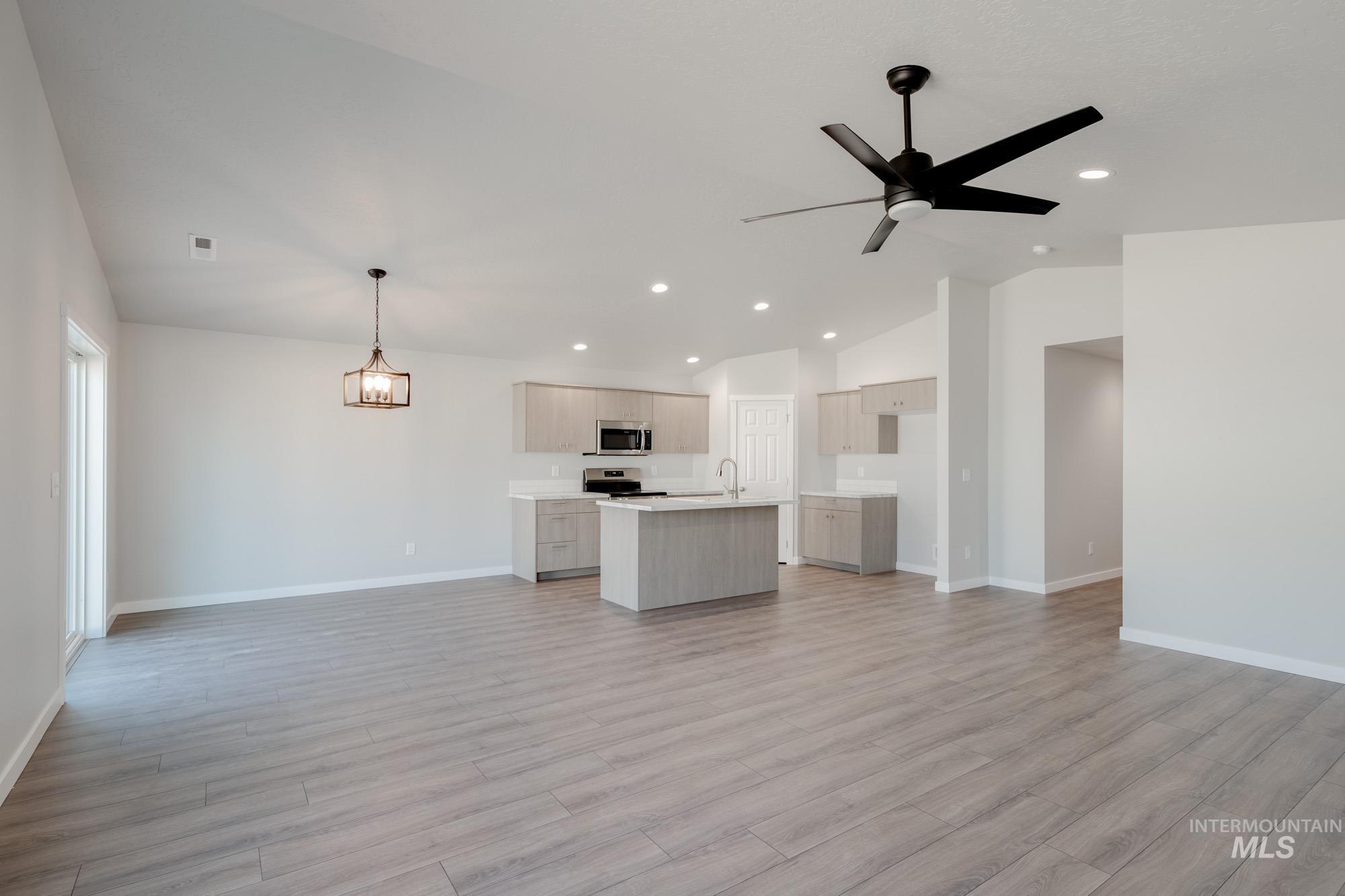 Kitchen featuring open floor plan, light countertops, vaulted ceiling, a center island with sink, and light wood-style floors