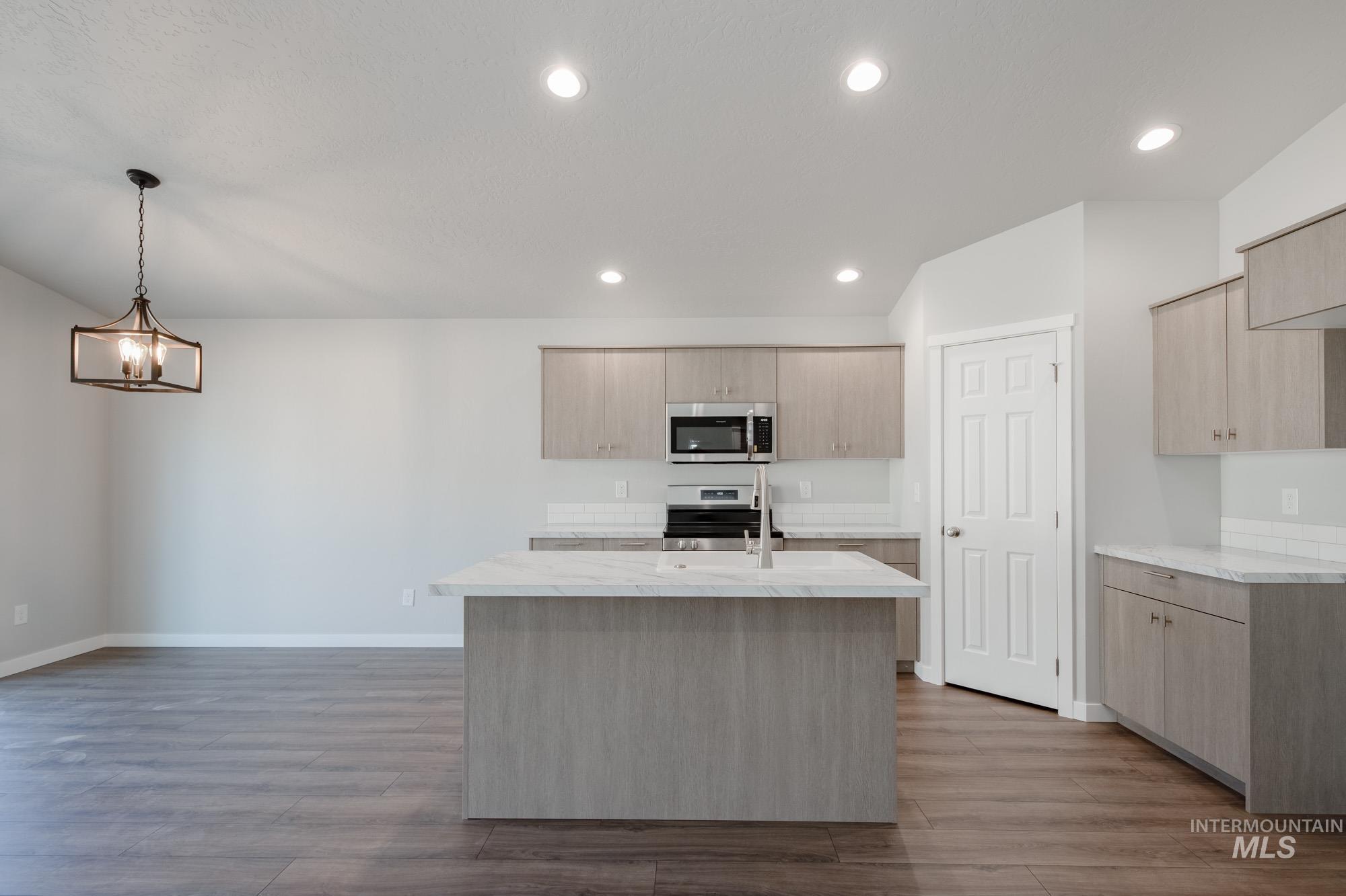 Kitchen featuring light brown cabinets, an island with sink, recessed lighting, pendant lighting, and dark wood-style flooring