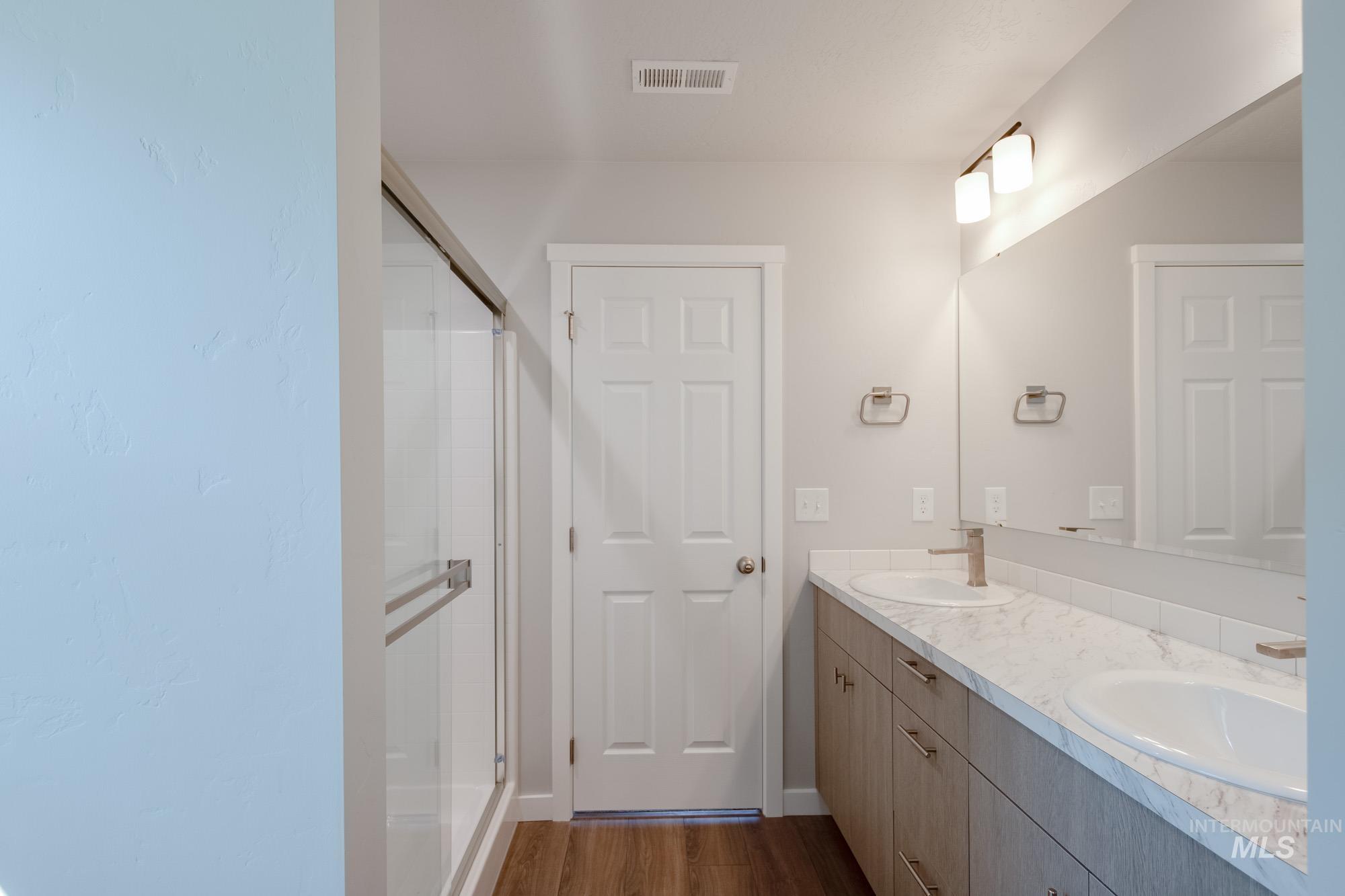 Full bath featuring dark wood-style flooring, a stall shower, and double vanity