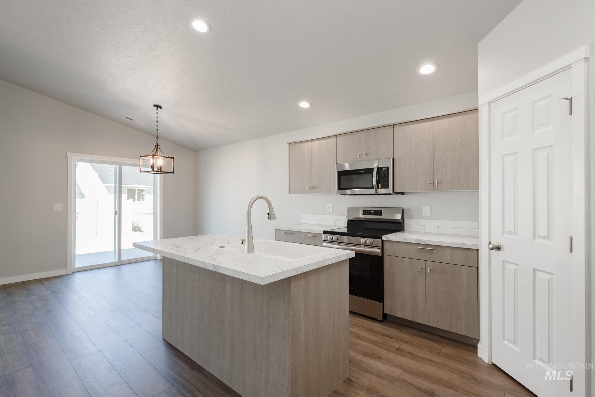 Kitchen featuring appliances with stainless steel finishes, light brown cabinets, decorative light fixtures, a kitchen island with sink, and recessed lighting