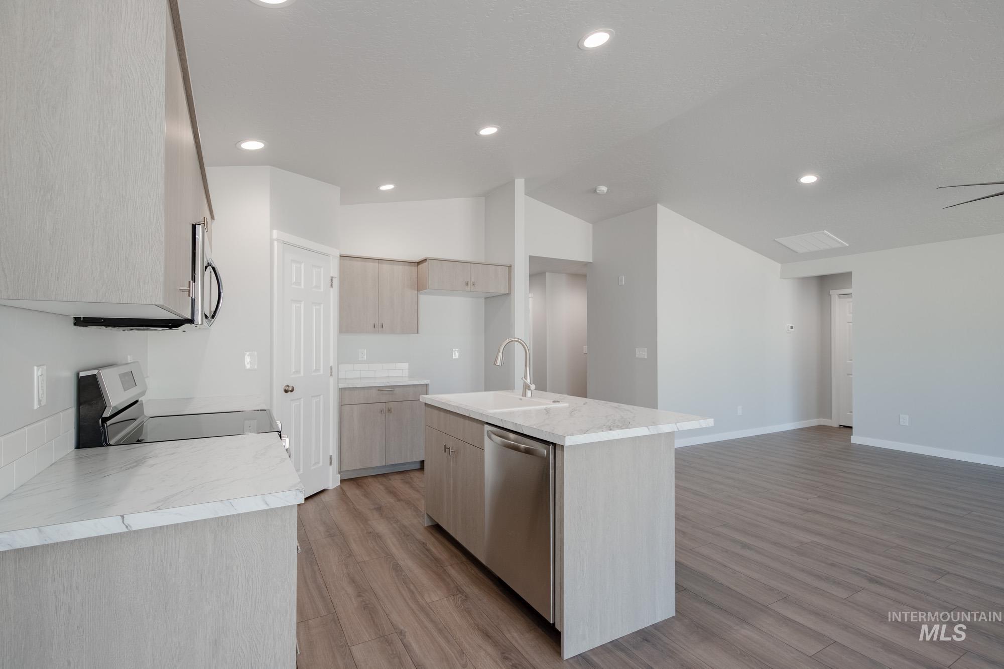 Kitchen featuring an island with sink, light wood finished floors, stainless steel appliances, recessed lighting, and light brown cabinetry
