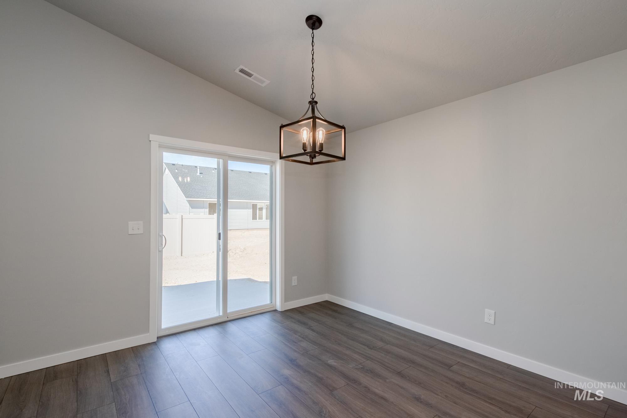 Spare room with dark wood finished floors, a chandelier, and lofted ceiling