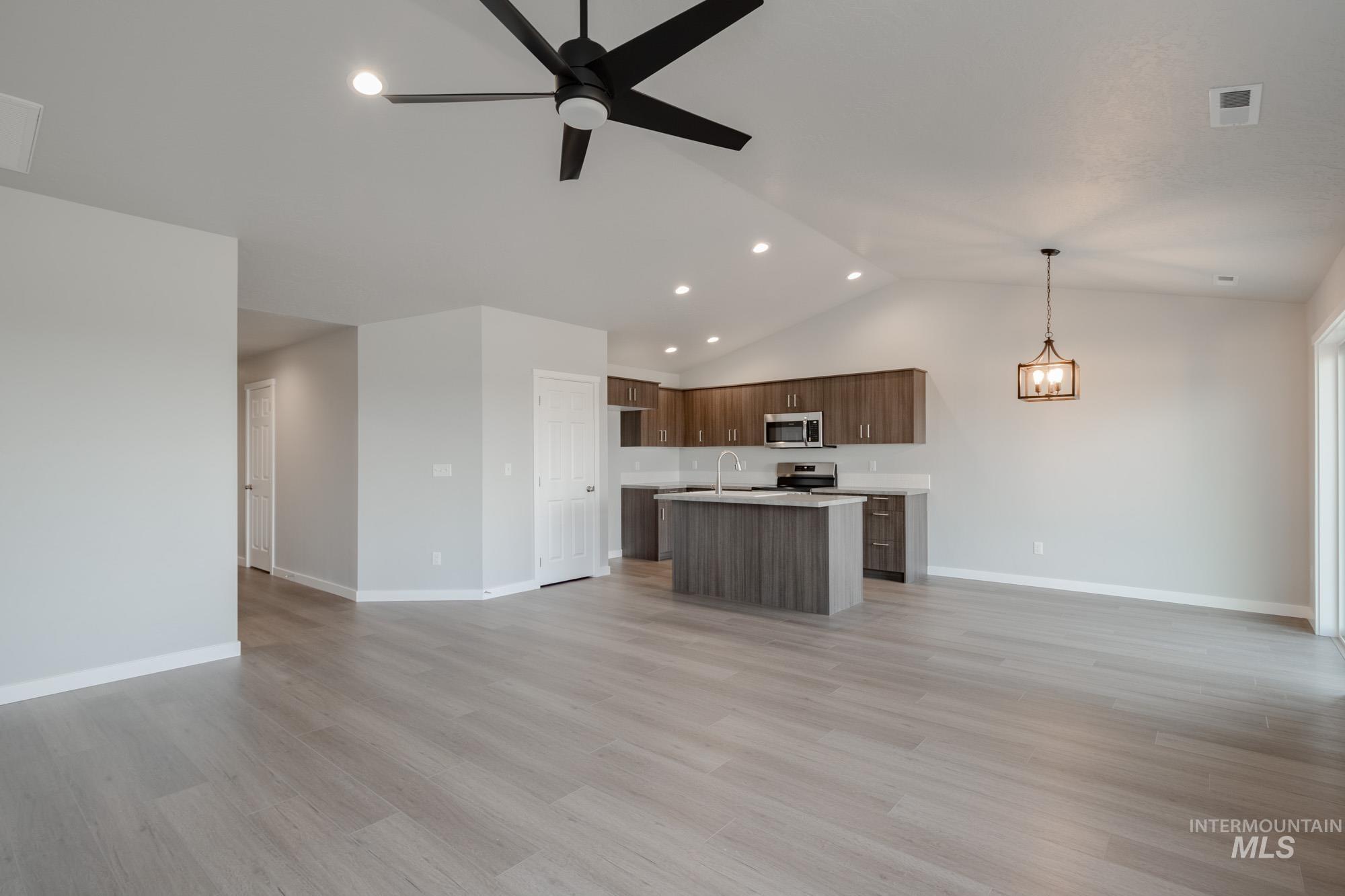 Kitchen with open floor plan, light countertops, light wood-type flooring, an island with sink, and lofted ceiling