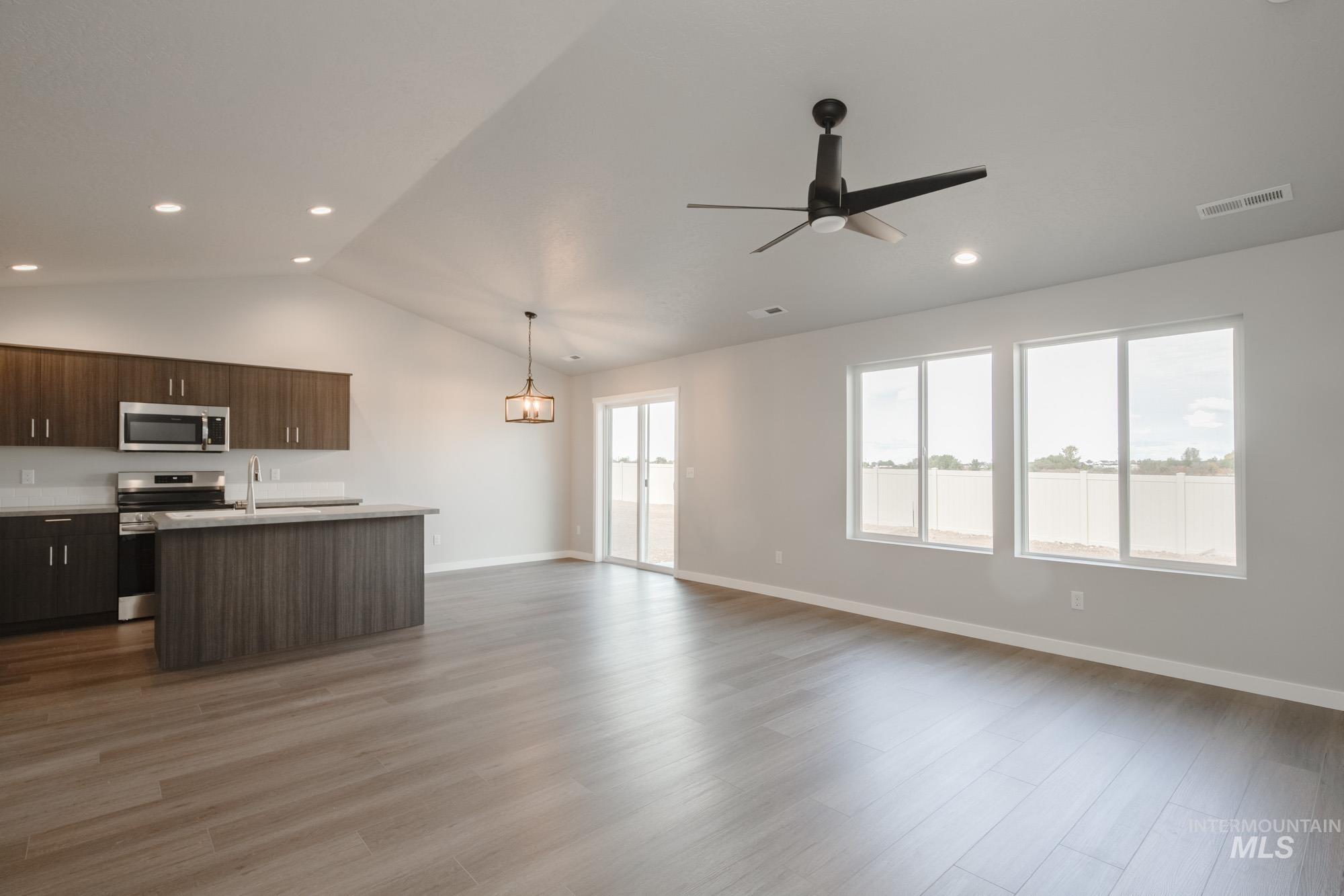 Kitchen with light countertops, open floor plan, a kitchen island with sink, stainless steel appliances, and lofted ceiling