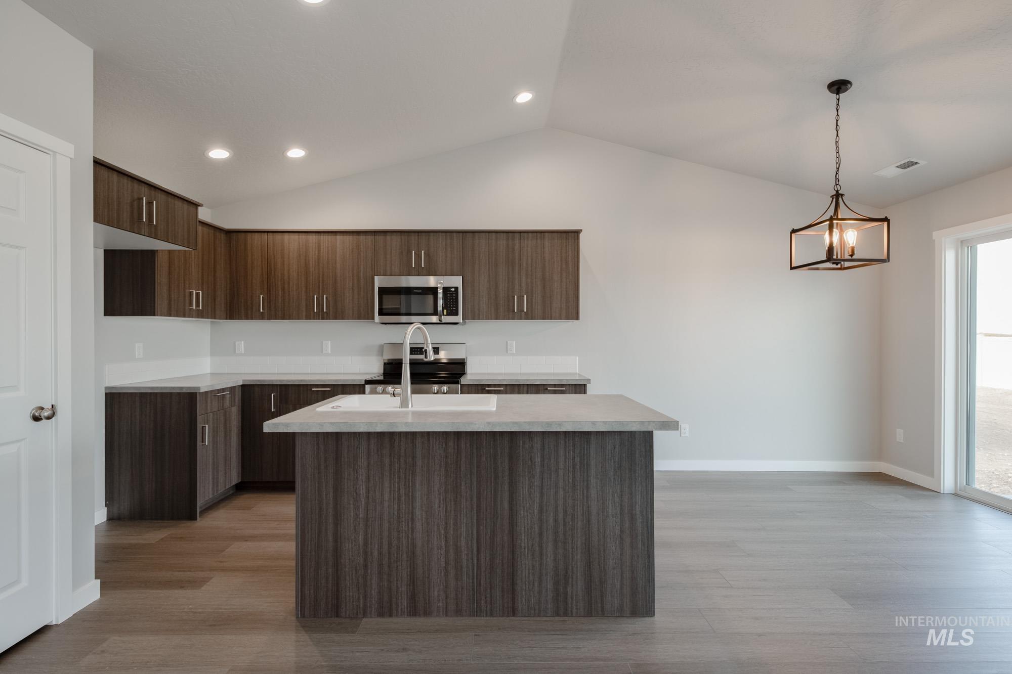 Kitchen featuring modern cabinets, stainless steel appliances, vaulted ceiling, light wood-type flooring, and pendant lighting