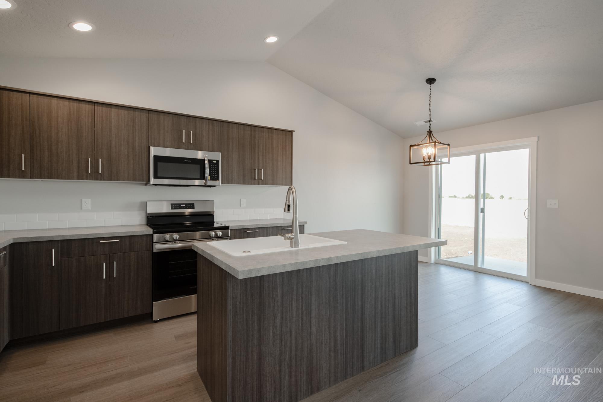 Kitchen featuring stainless steel appliances, dark brown cabinets, light wood-style flooring, a kitchen island with sink, and lofted ceiling