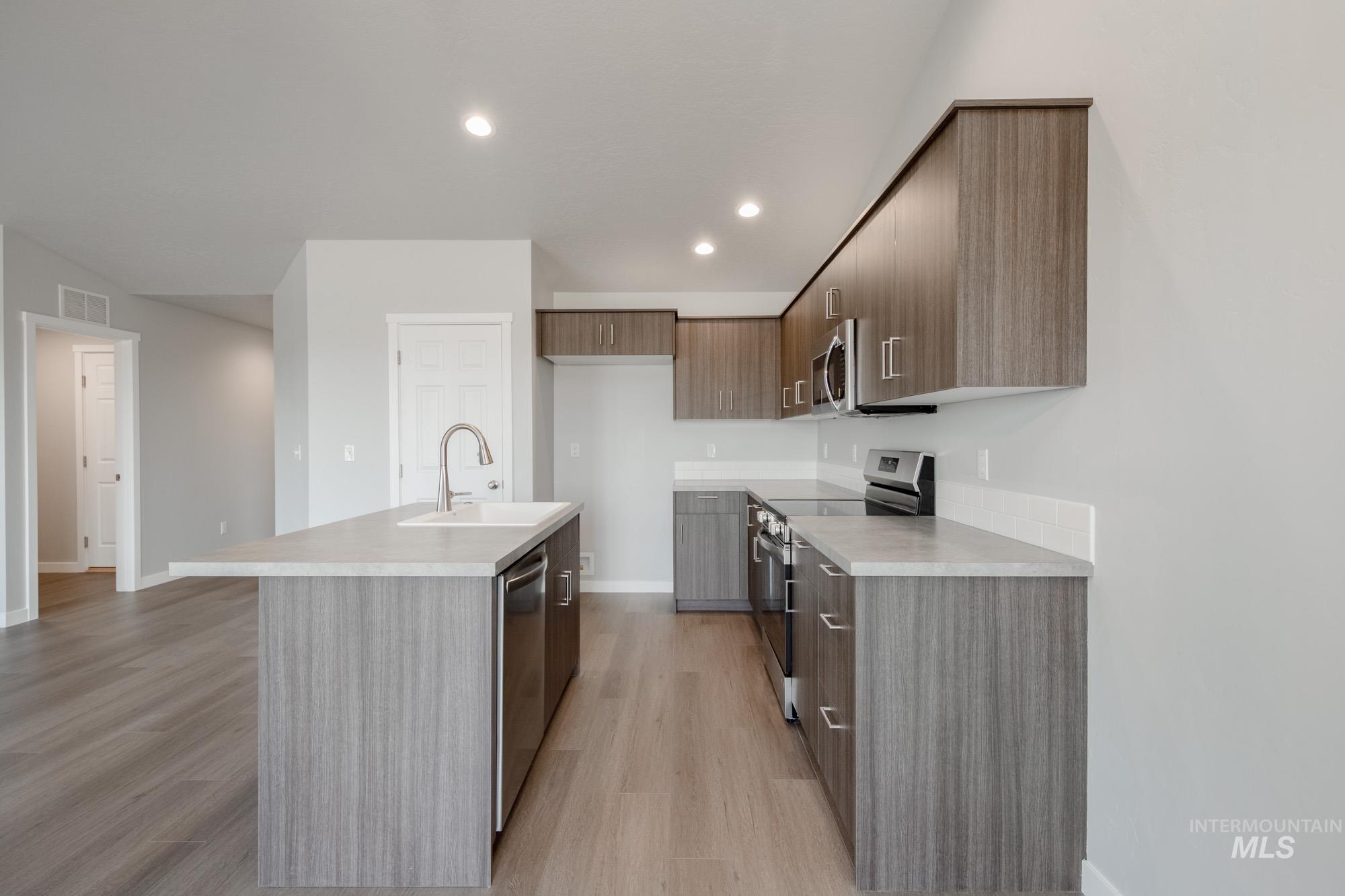 Kitchen featuring modern cabinets, stainless steel appliances, light countertops, a center island with sink, and recessed lighting