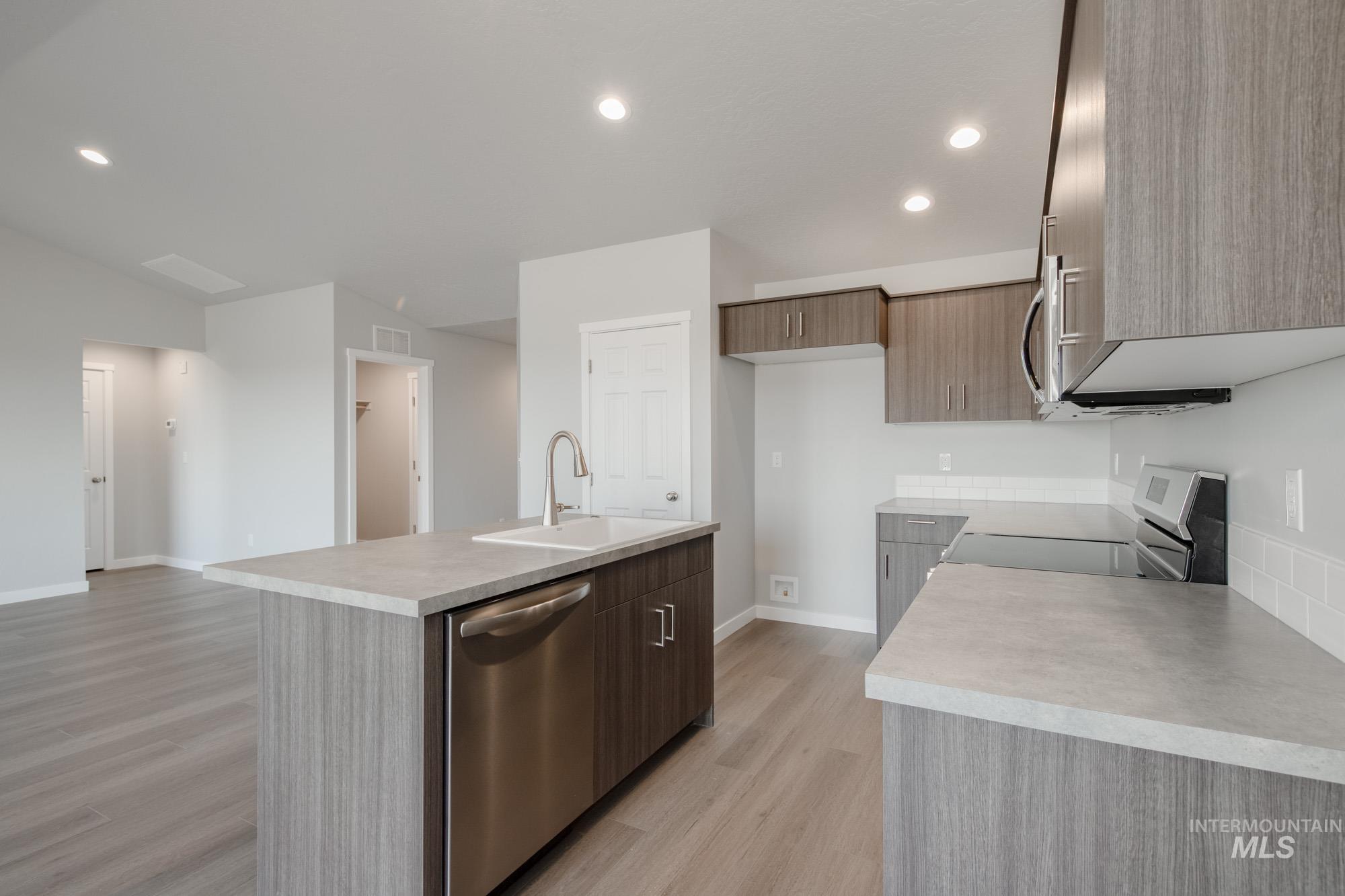 Kitchen featuring light wood finished floors, appliances with stainless steel finishes, recessed lighting, a center island with sink, and light countertops