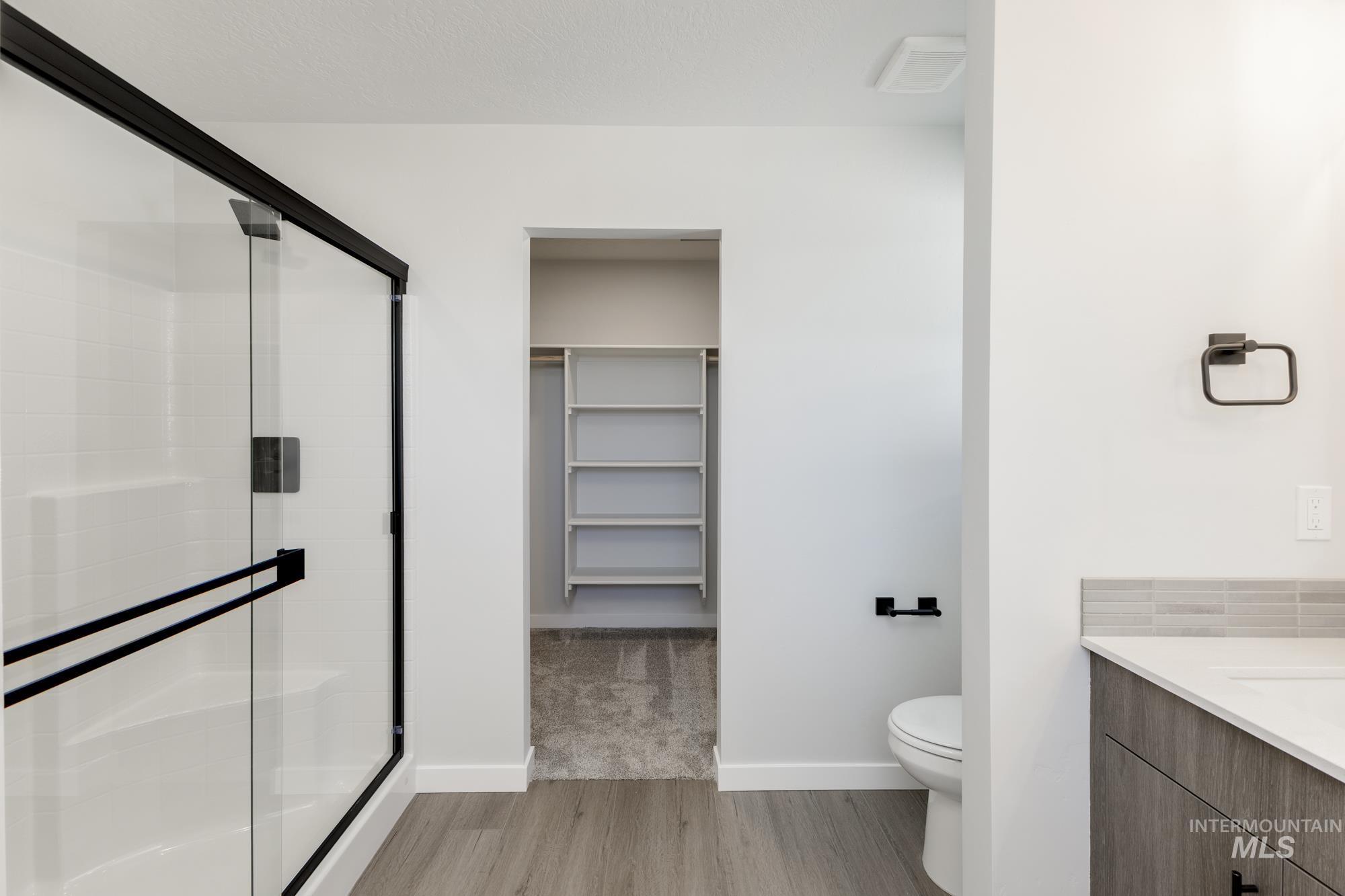 Full bath featuring vanity, a stall shower, light wood-style floors, and a walk in closet