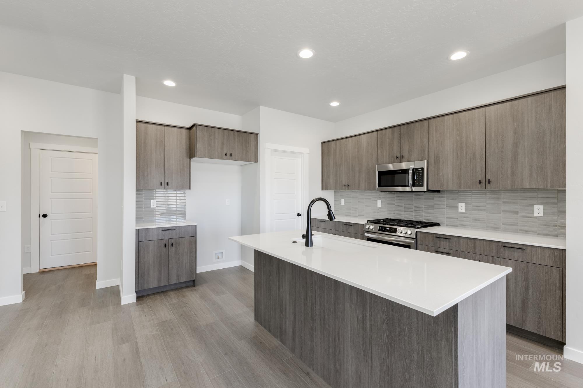 Kitchen featuring decorative backsplash, stainless steel appliances, modern cabinets, light stone counters, and light wood-style flooring