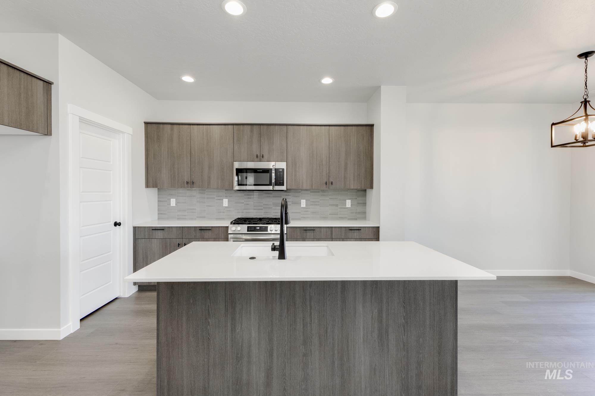 Kitchen with modern cabinets, backsplash, a center island with sink, appliances with stainless steel finishes, and light wood-style floors