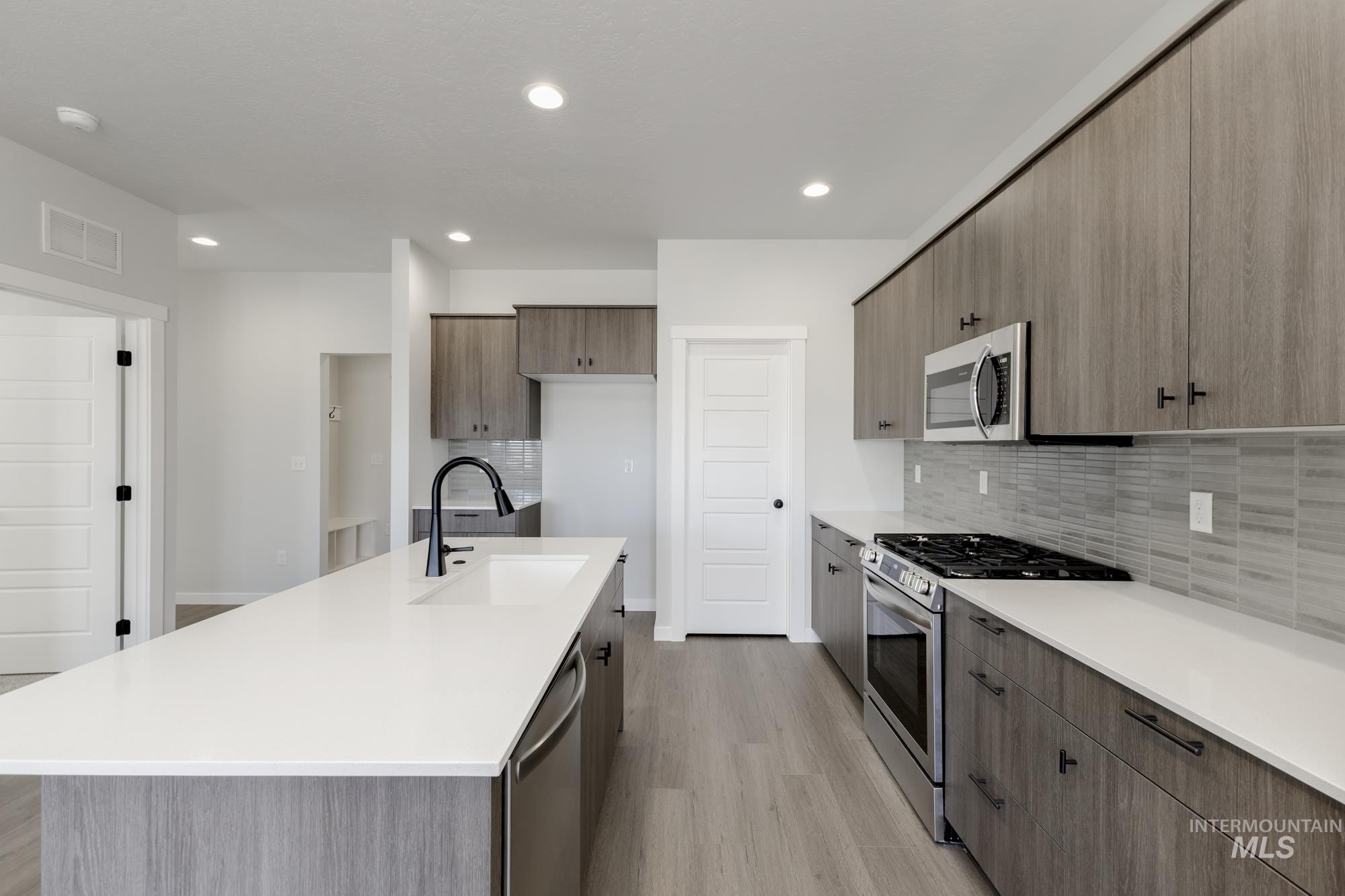 Kitchen featuring stainless steel appliances, decorative backsplash, light wood-type flooring, light stone counters, and recessed lighting