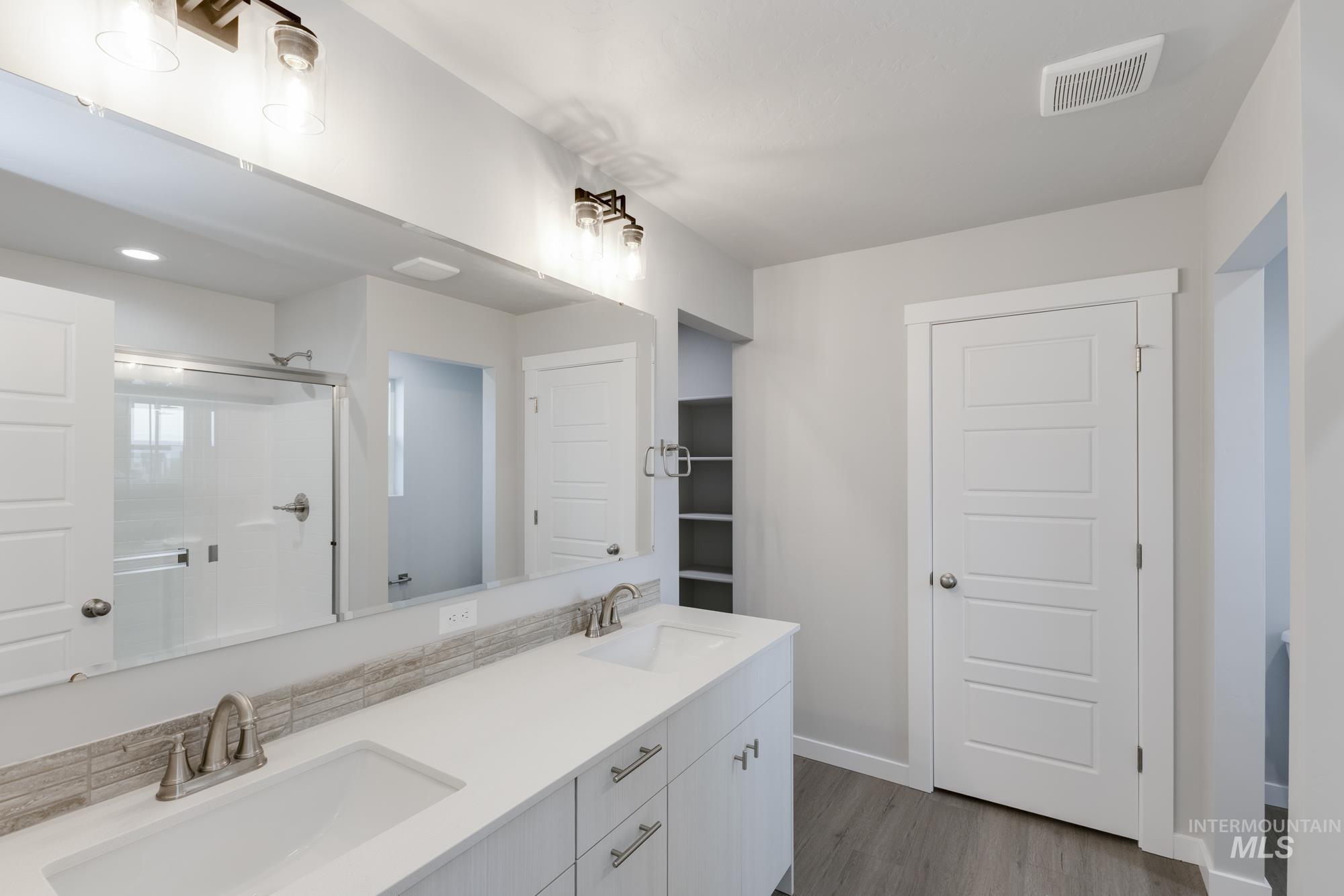 Bathroom featuring double vanity, dark wood-type flooring, and a shower stall