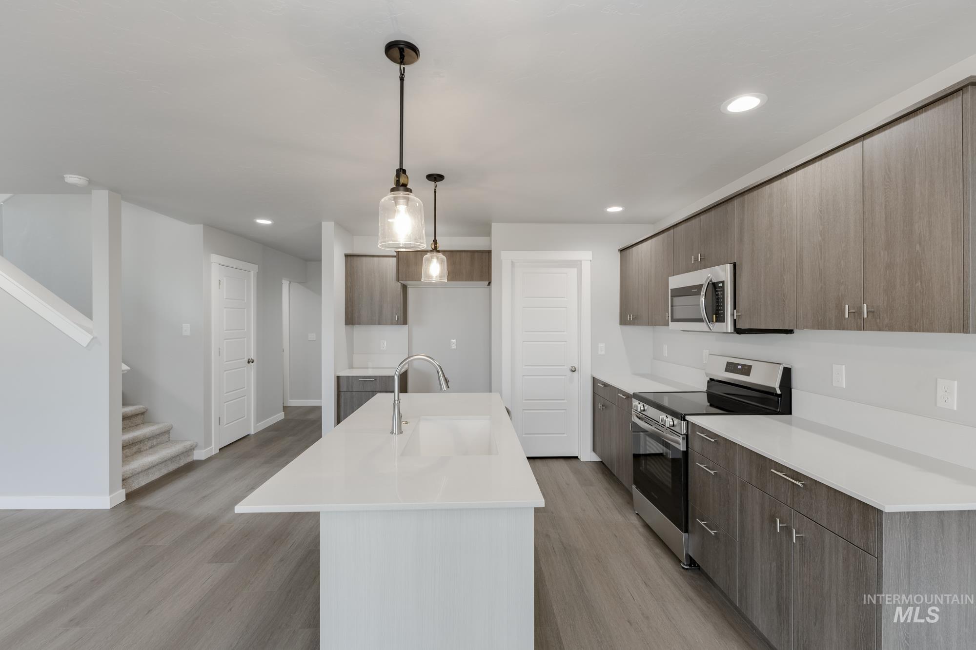 Kitchen featuring stainless steel appliances, an island with sink, hanging light fixtures, light wood finished floors, and modern cabinets