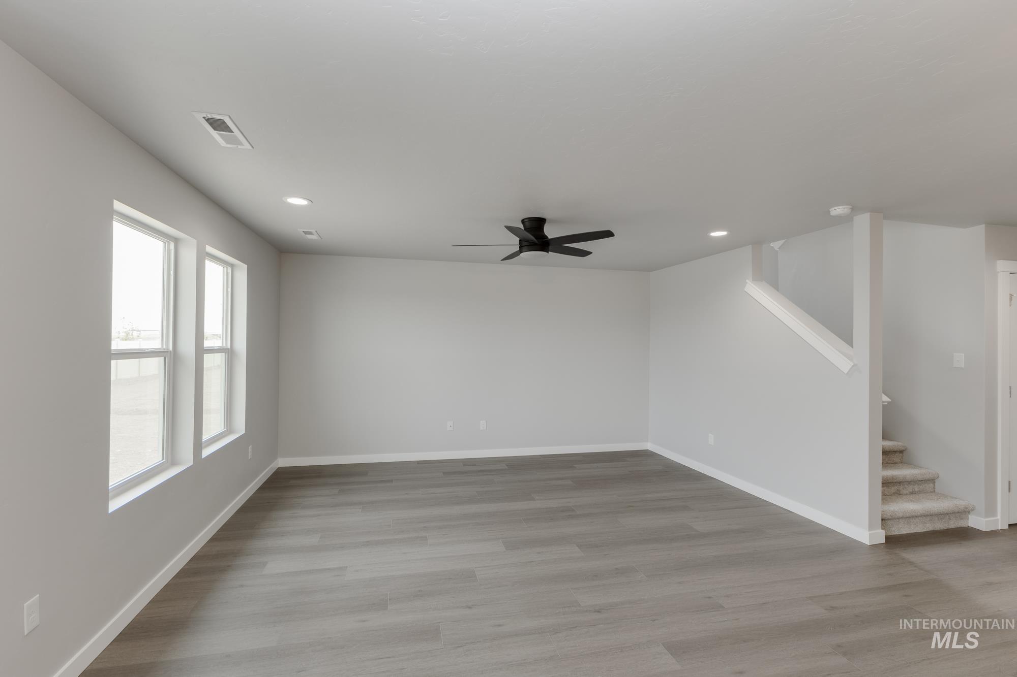 Unfurnished living room with light wood finished floors, a ceiling fan, recessed lighting, and stairway