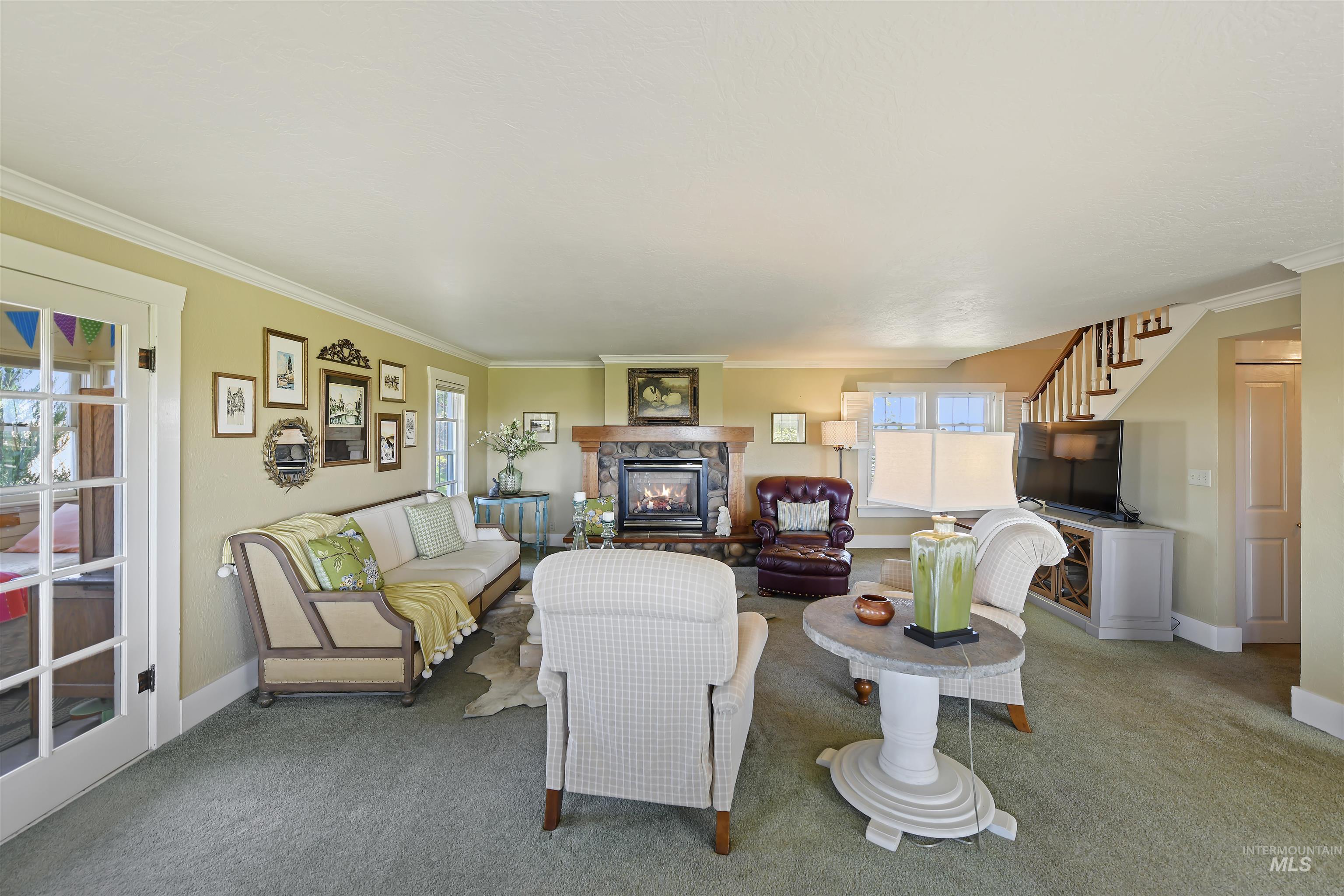 Living room featuring crown molding, stairs, carpet floors, healthy amount of natural light, and a fireplace