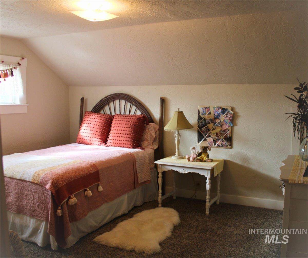 Bedroom featuring a textured ceiling, a textured wall, carpet flooring, and lofted ceiling