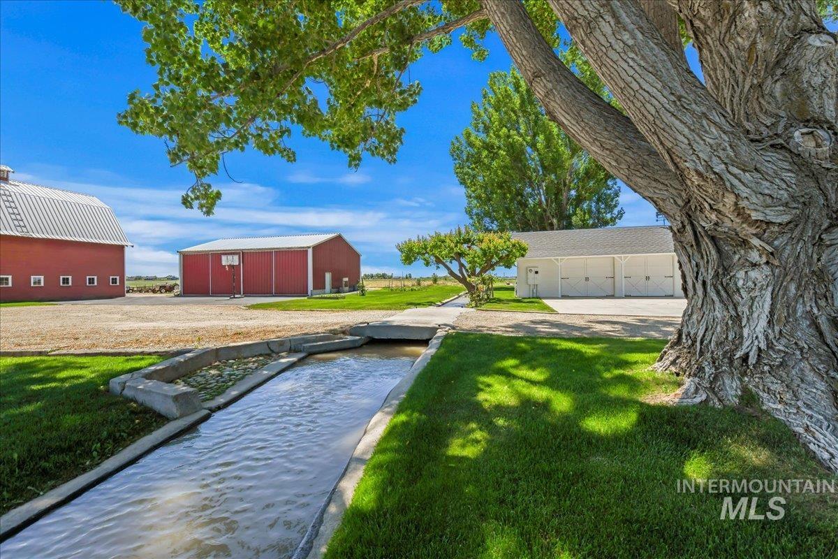 View of green lawn featuring an outdoor structure, a pole building, a detached garage, and a garden pond