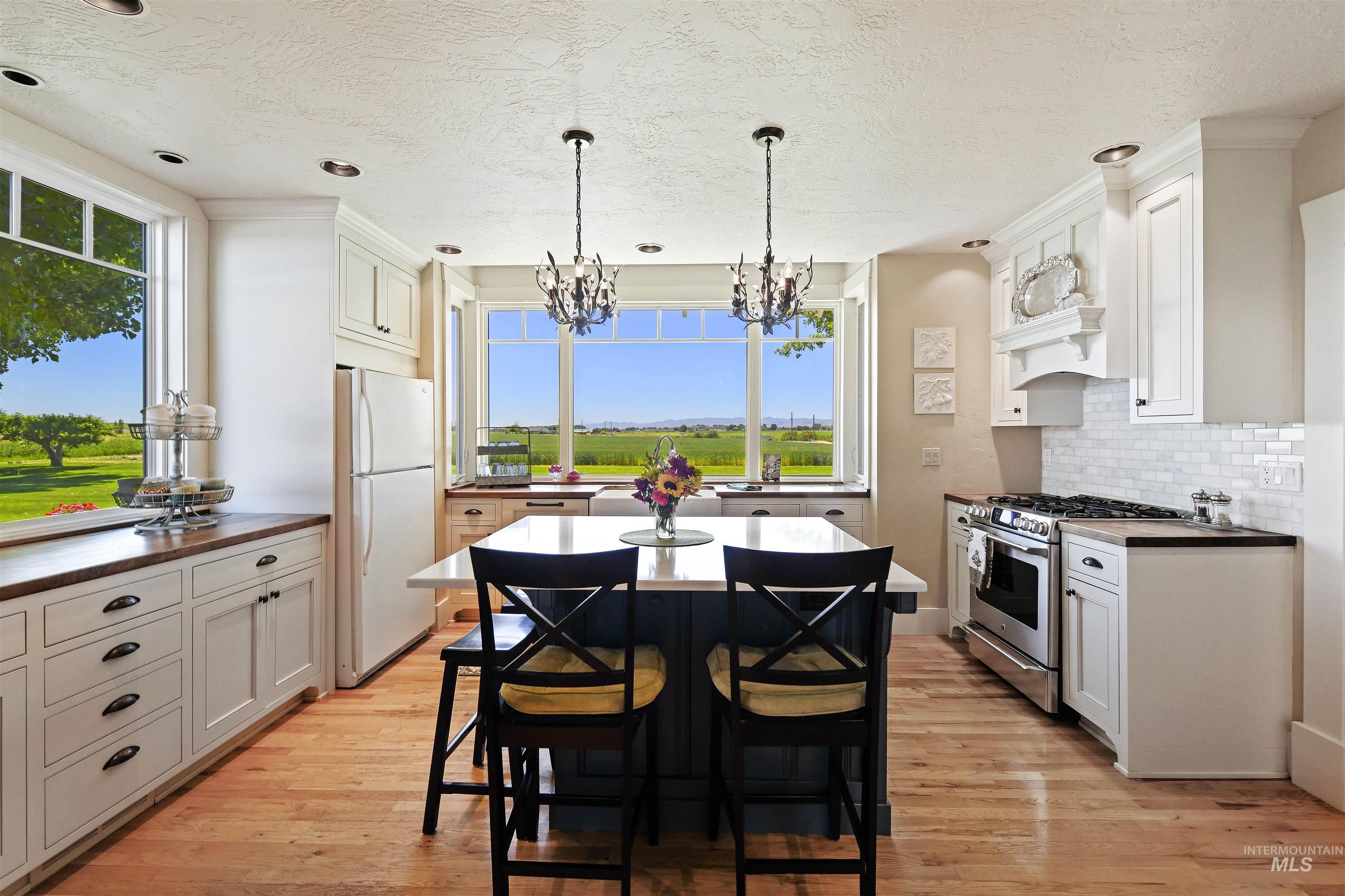 Kitchen featuring stainless steel range with gas stovetop, freestanding refrigerator, backsplash, light wood-type flooring, and white cabinets