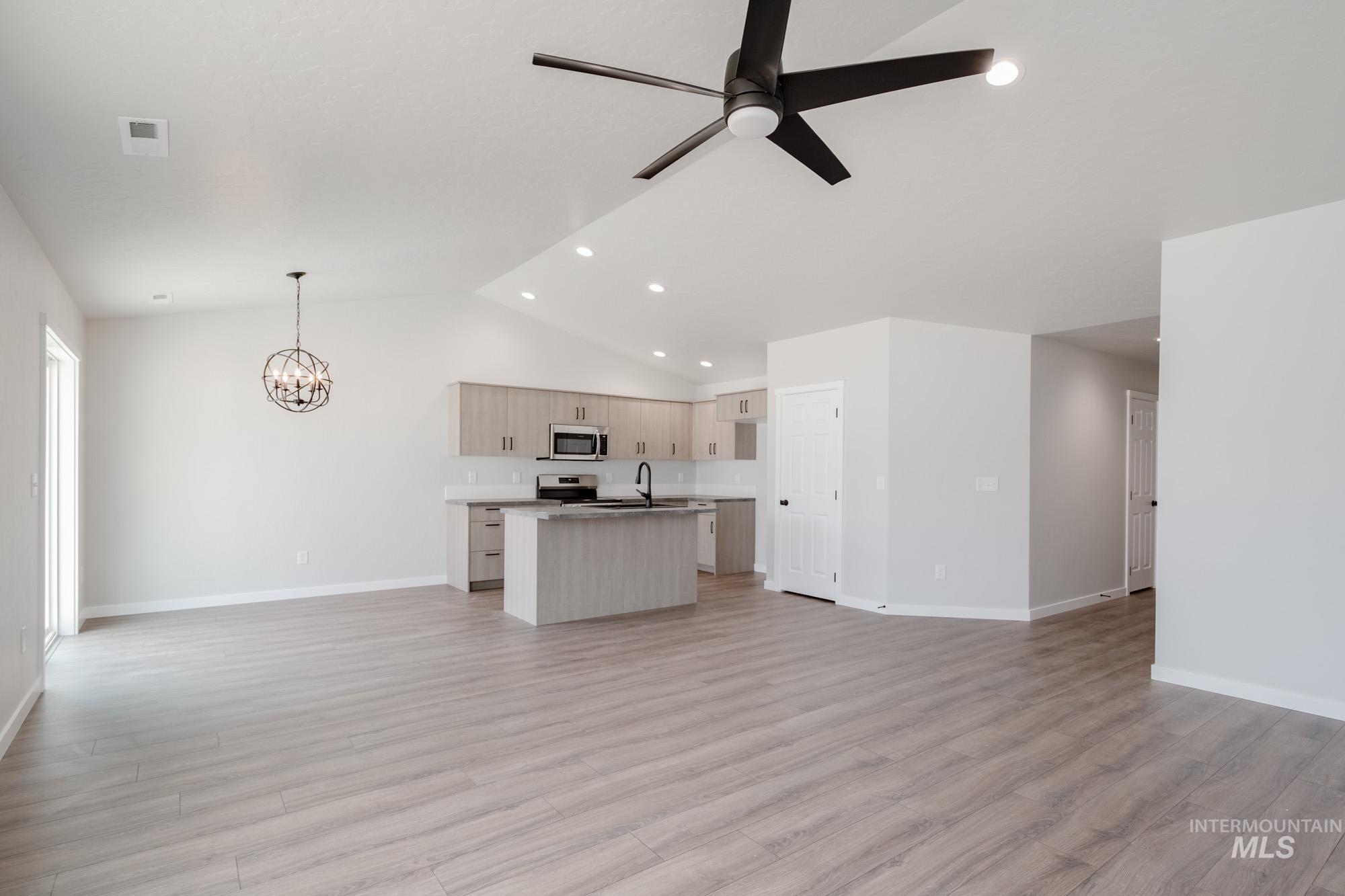 Kitchen with open floor plan, an island with sink, light wood-style flooring, a chandelier, and lofted ceiling