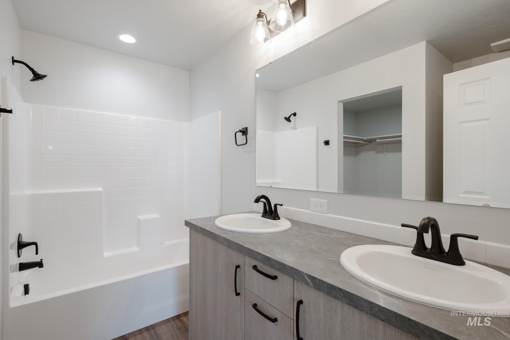 Full bathroom with double vanity, shower / washtub combination, a spacious closet, dark wood-style floors, and recessed lighting