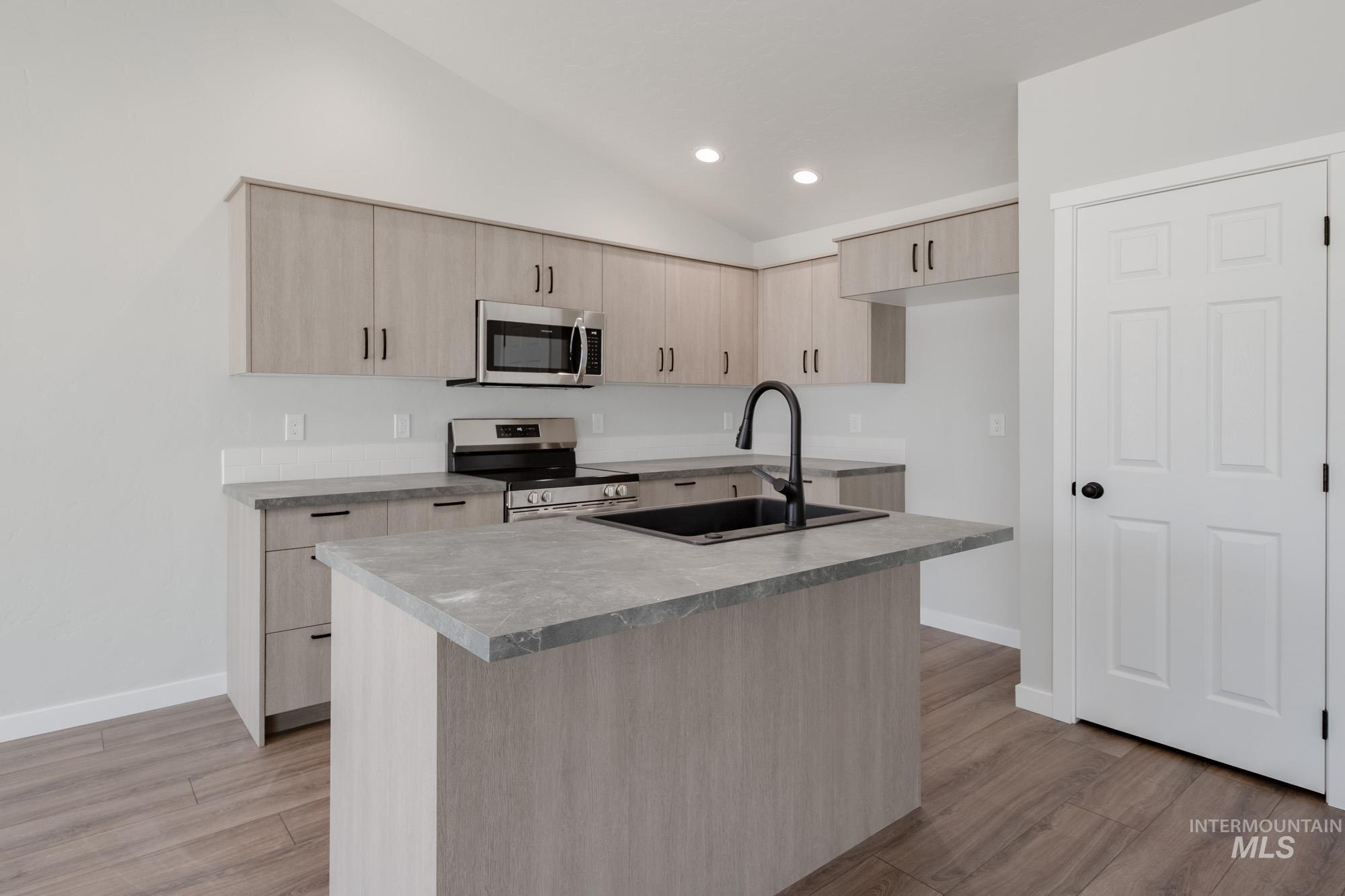 Kitchen featuring light brown cabinetry, recessed lighting, vaulted ceiling, appliances with stainless steel finishes, and modern cabinets