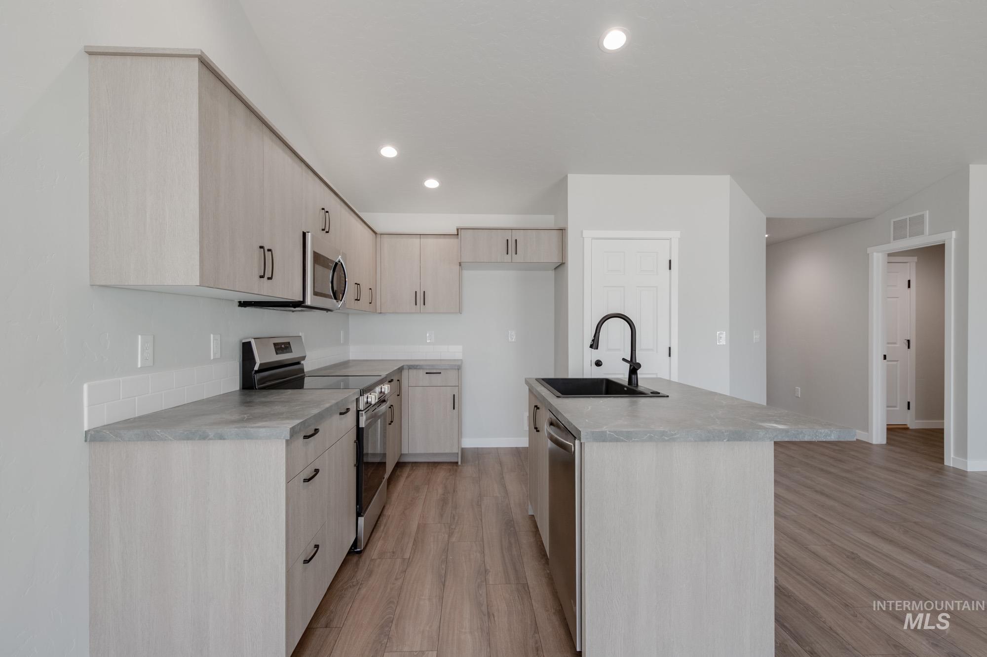 Kitchen with light brown cabinetry, stainless steel appliances, recessed lighting, light wood-type flooring, and a center island with sink