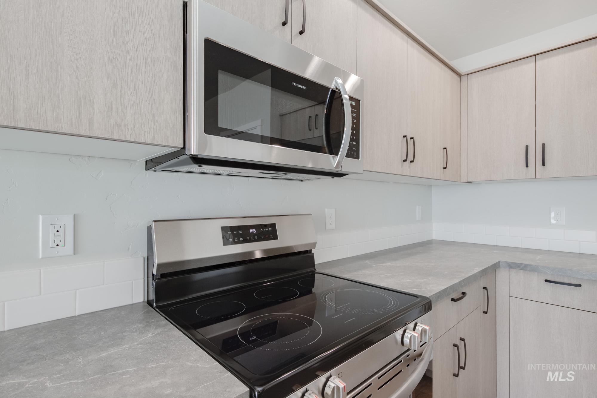 Kitchen with appliances with stainless steel finishes, light brown cabinetry, and modern cabinets