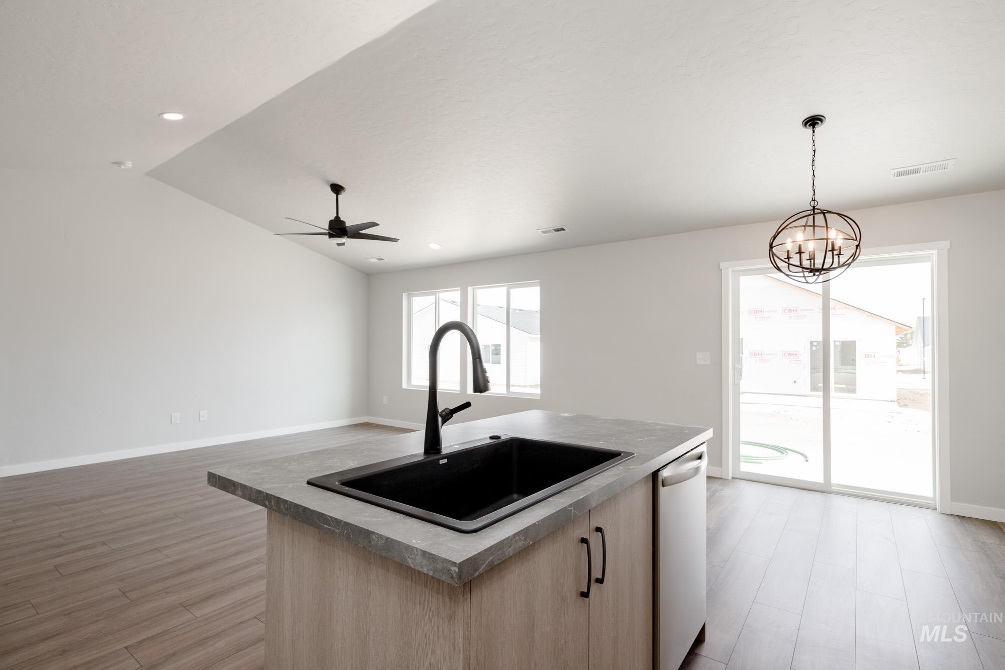 Kitchen featuring light brown cabinets, open floor plan, a center island with sink, light wood-style floors, and hanging light fixtures