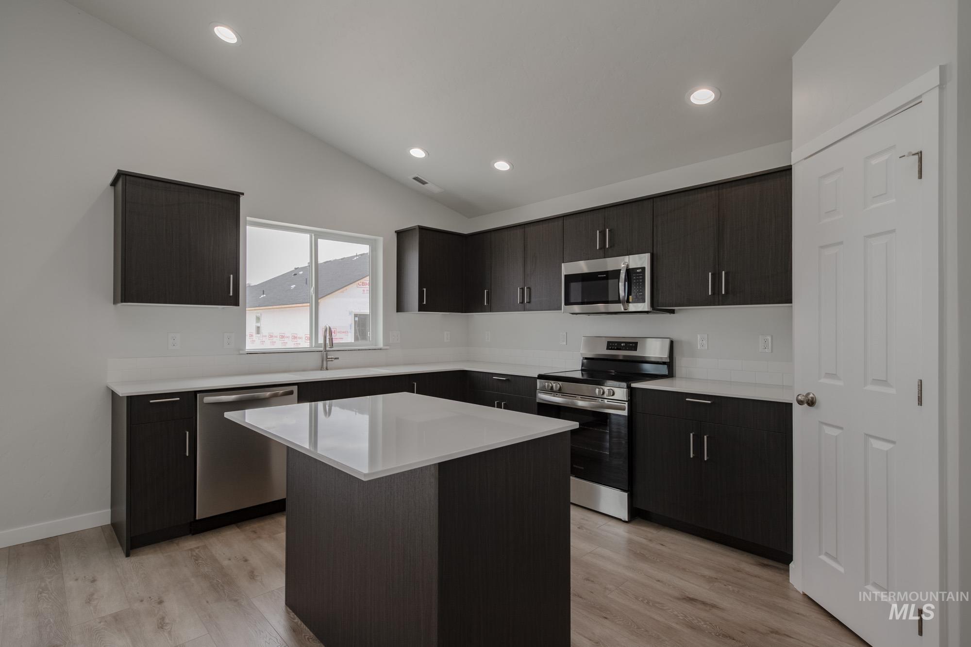 Kitchen with stainless steel appliances, vaulted ceiling, light wood finished floors, a kitchen island, and recessed lighting