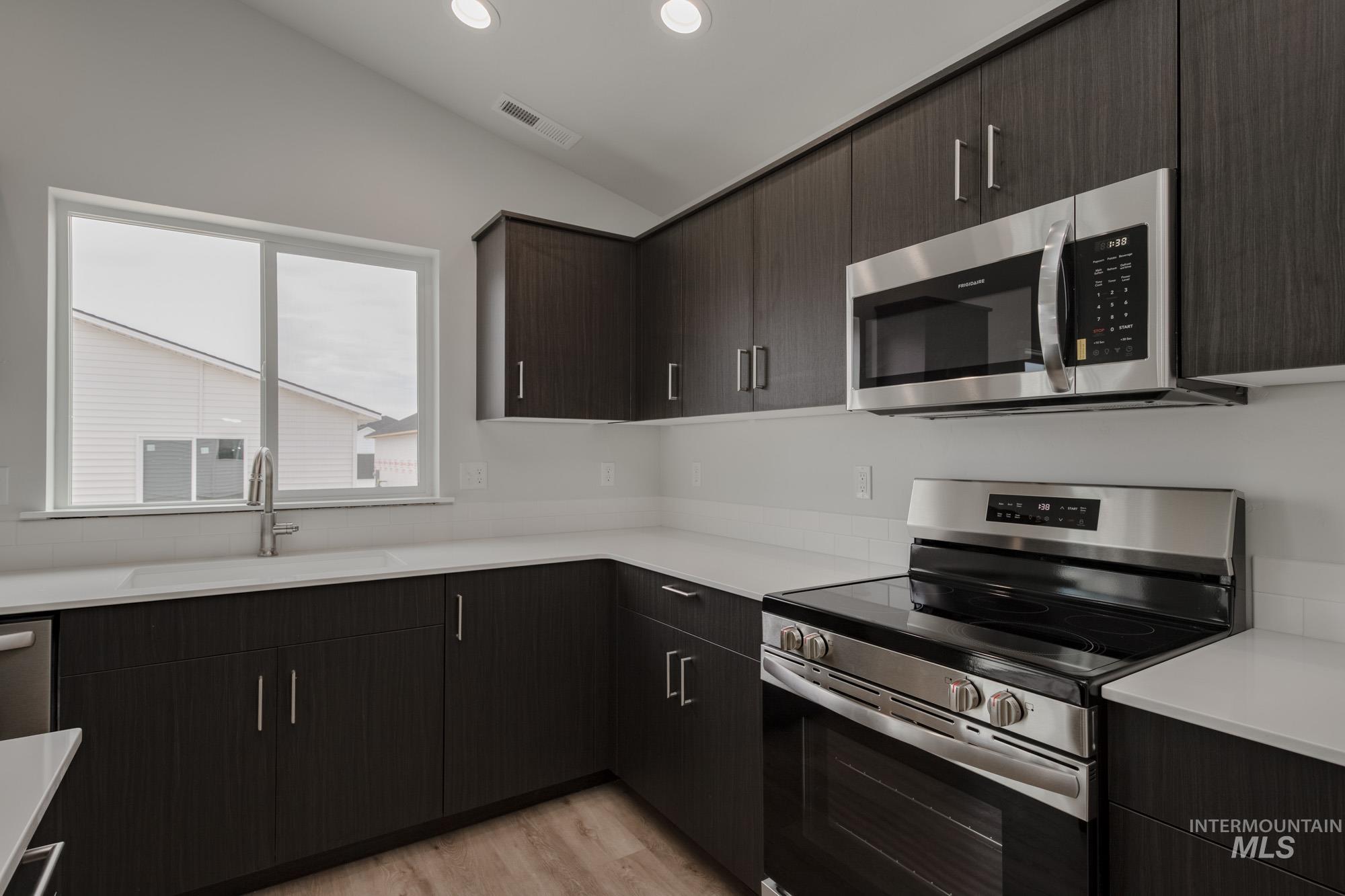 Kitchen featuring stainless steel appliances, modern cabinets, light wood-style flooring, dark brown cabinetry, and recessed lighting