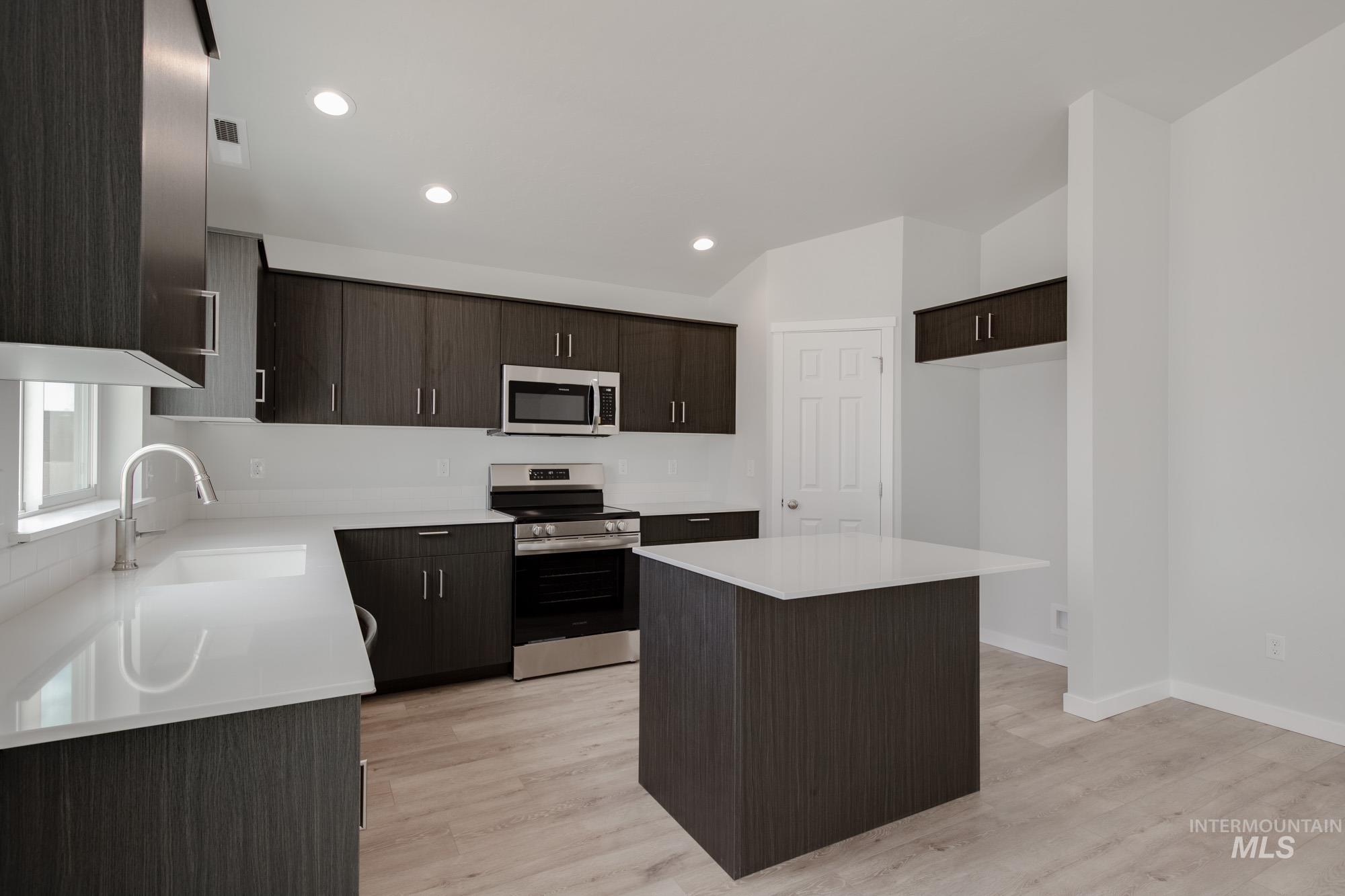 Kitchen with dark brown cabinets, stainless steel appliances, a kitchen island, light wood-type flooring, and recessed lighting