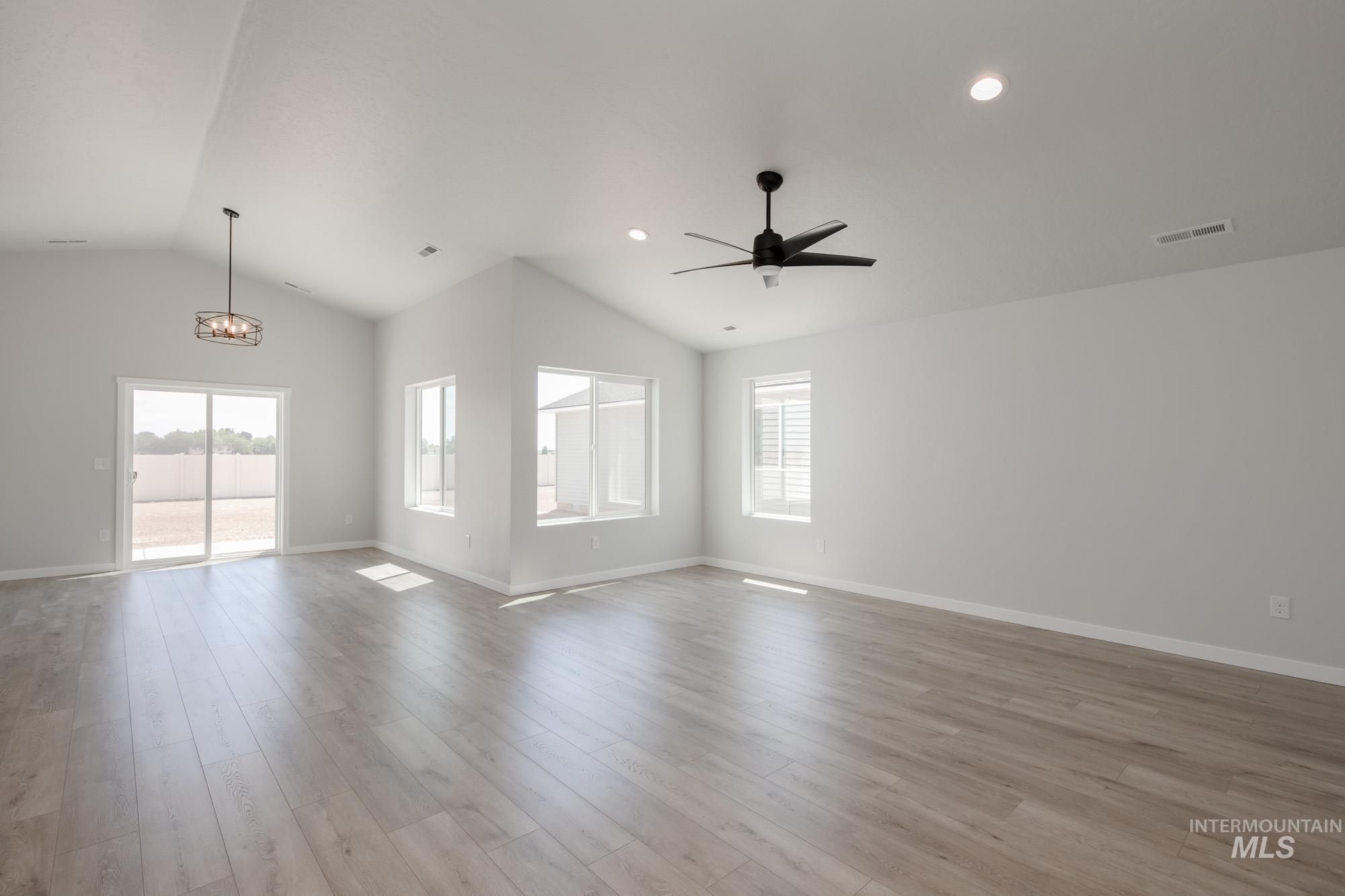 Unfurnished living room featuring healthy amount of natural light, vaulted ceiling, light wood-style floors, a chandelier, and ceiling fan