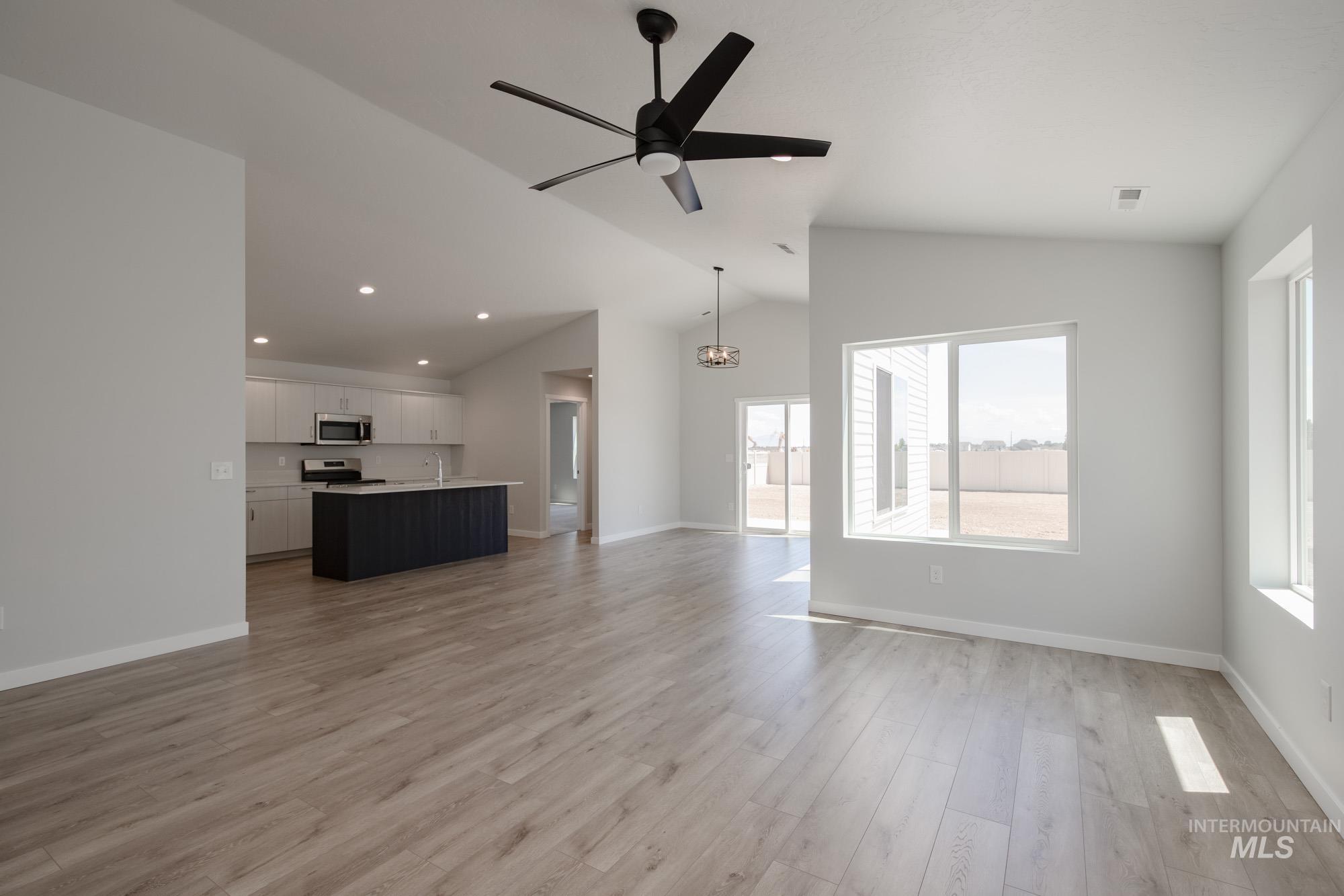 Unfurnished living room with light wood-type flooring, vaulted ceiling, ceiling fan, a chandelier, and recessed lighting