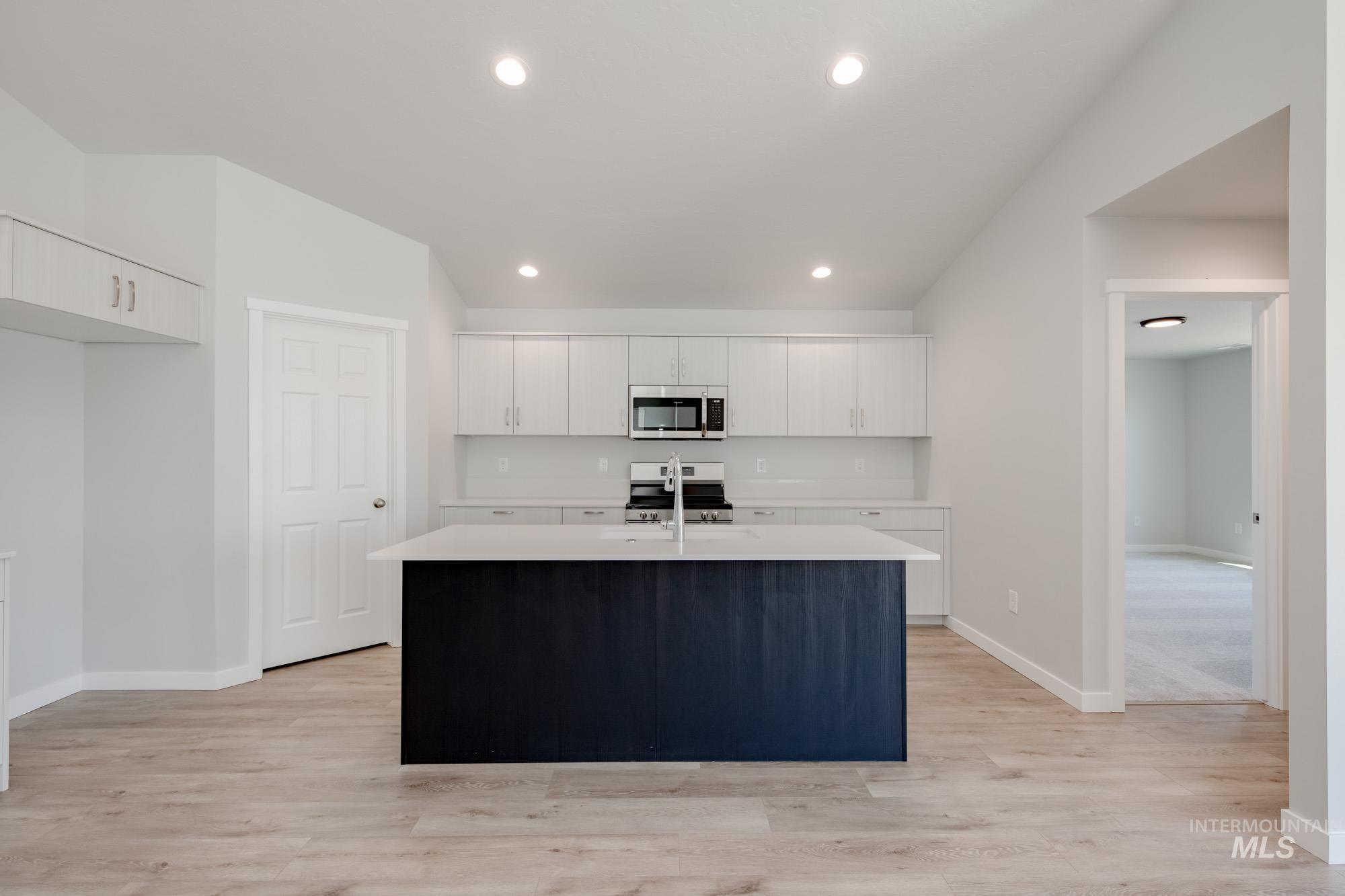 Kitchen with an island with sink, white cabinets, stainless steel appliances, light wood-style floors, and recessed lighting