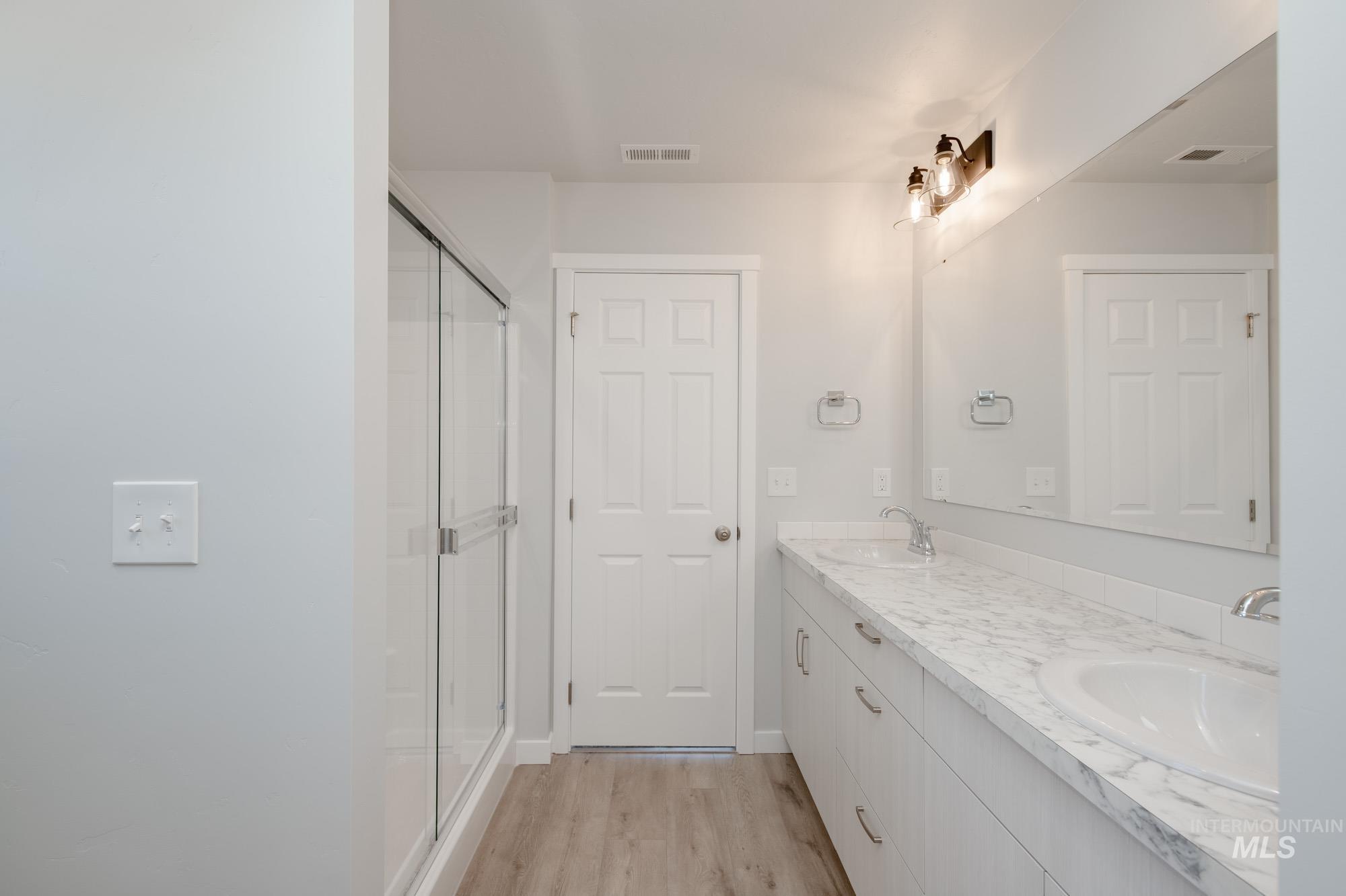 Full bathroom featuring light wood finished floors, a stall shower, and double vanity