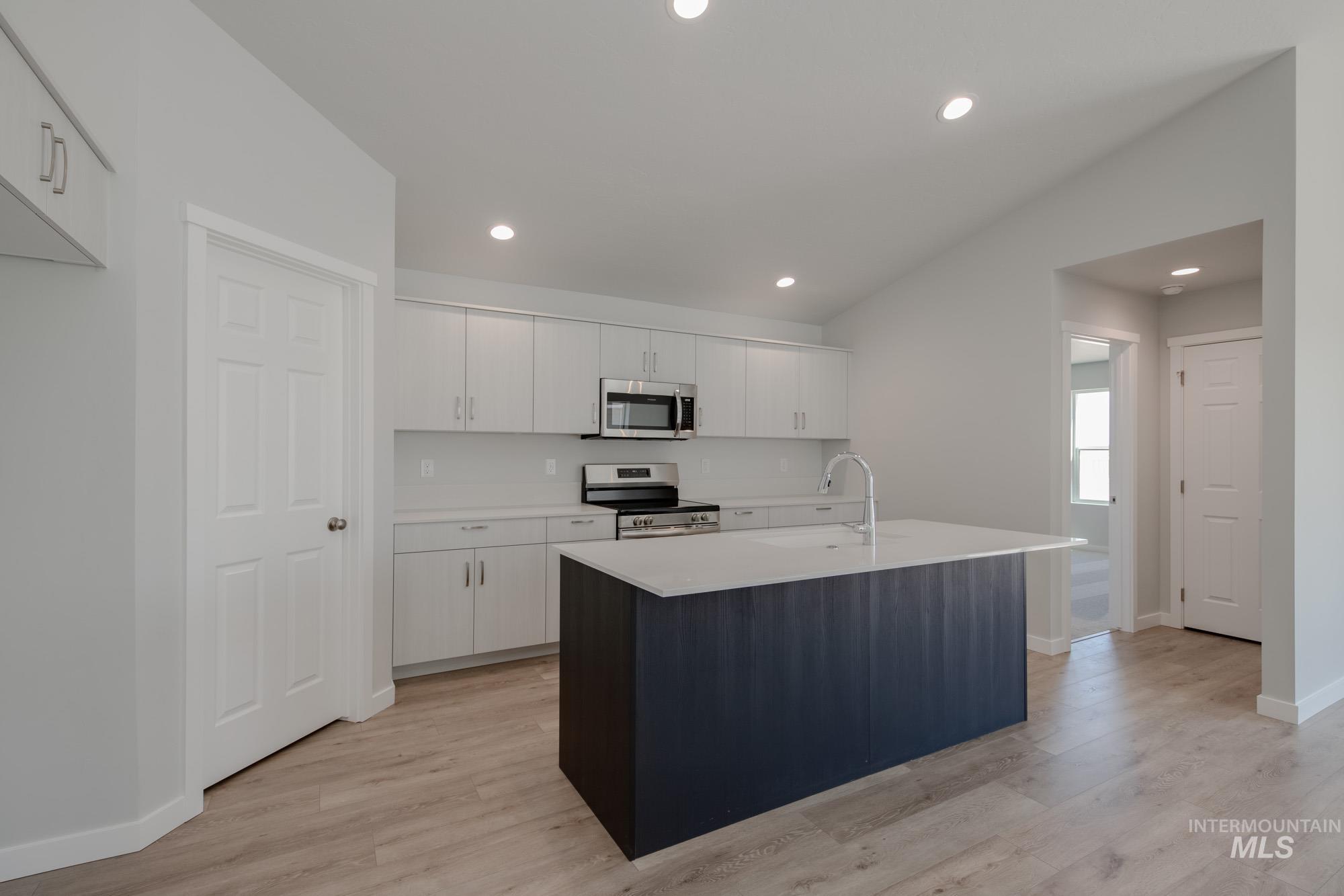 Kitchen with a center island with sink, recessed lighting, appliances with stainless steel finishes, white cabinets, and light wood-style floors