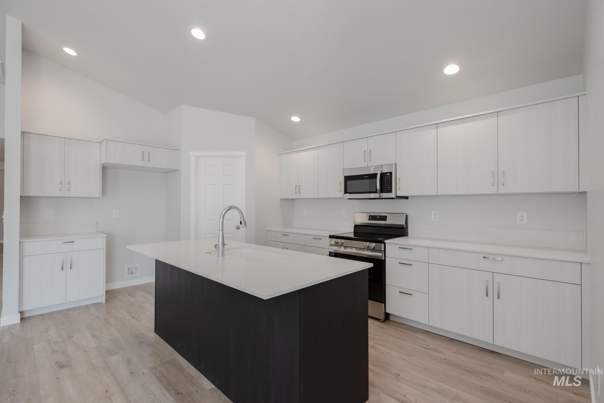 Kitchen with appliances with stainless steel finishes, white cabinets, light wood finished floors, an island with sink, and dark cabinets