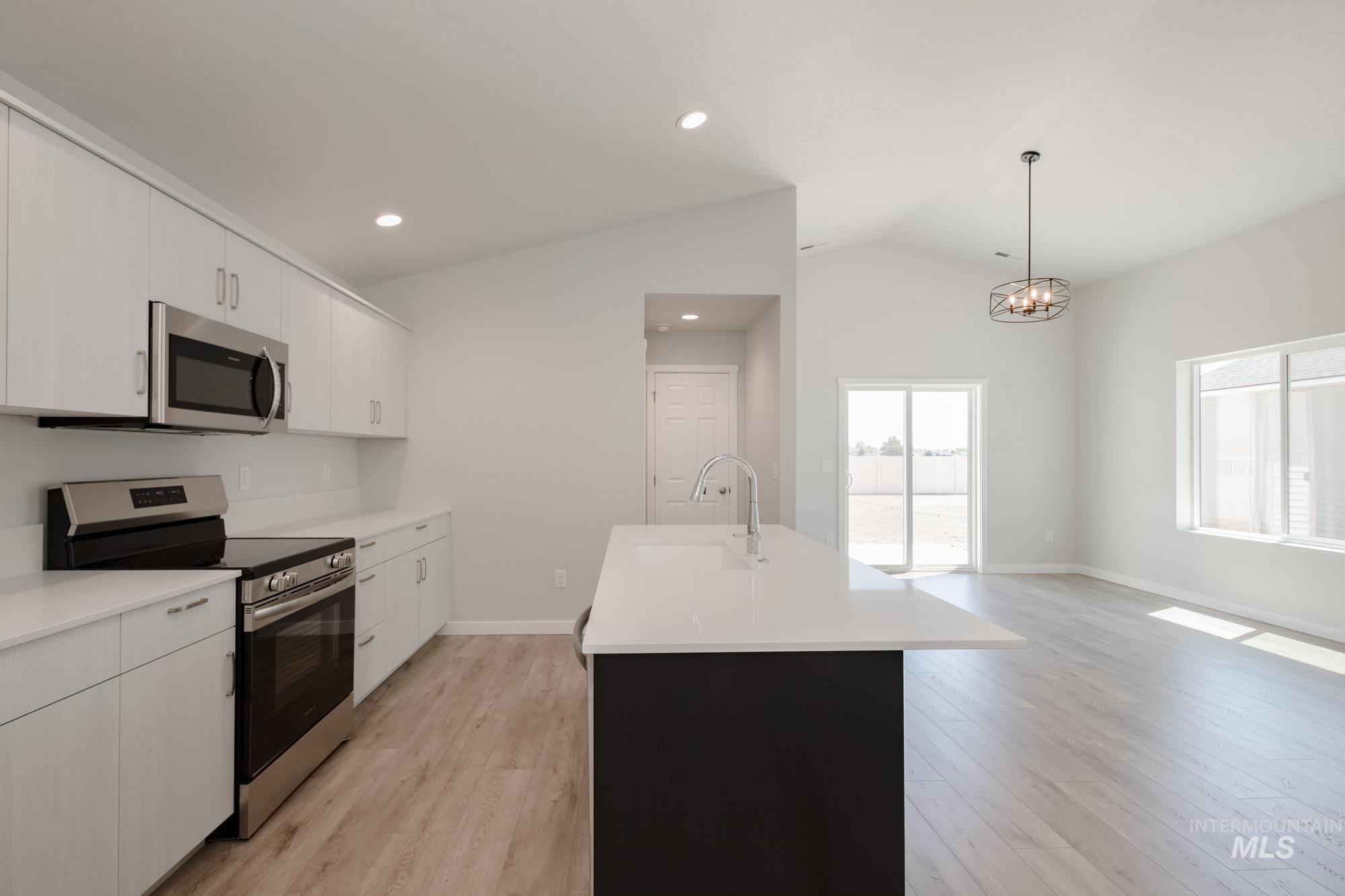 Kitchen featuring stainless steel appliances, lofted ceiling, a kitchen island with sink, light wood finished floors, and white cabinets