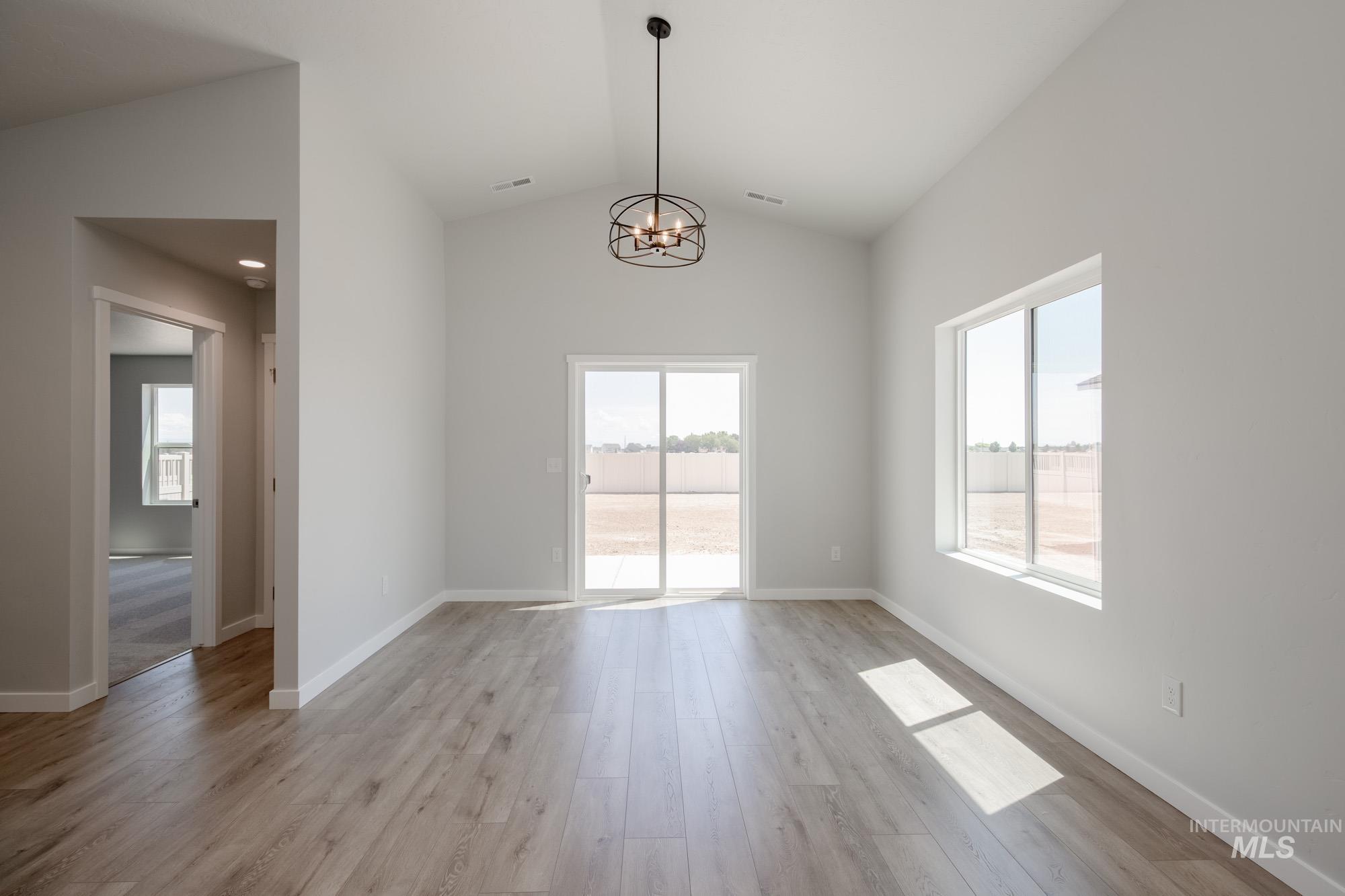 Unfurnished dining area with vaulted ceiling, a chandelier, healthy amount of natural light, and light wood-style flooring