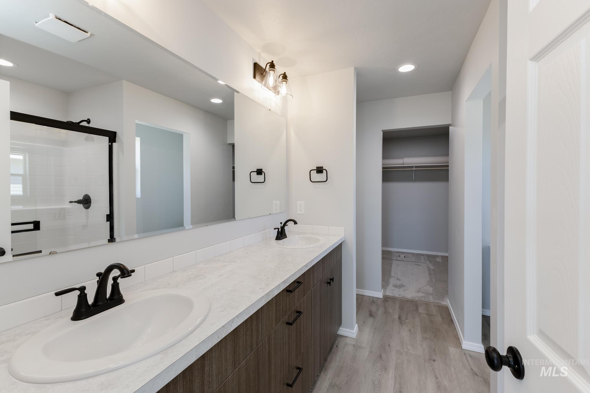 Full bathroom featuring a walk in closet, a shower stall, double vanity, light wood finished floors, and recessed lighting