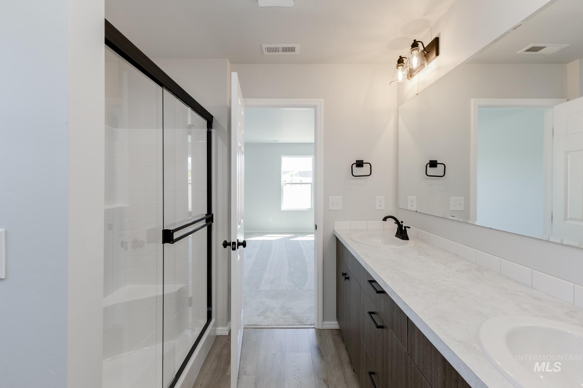 Bathroom featuring double vanity, a stall shower, and light wood-style floors