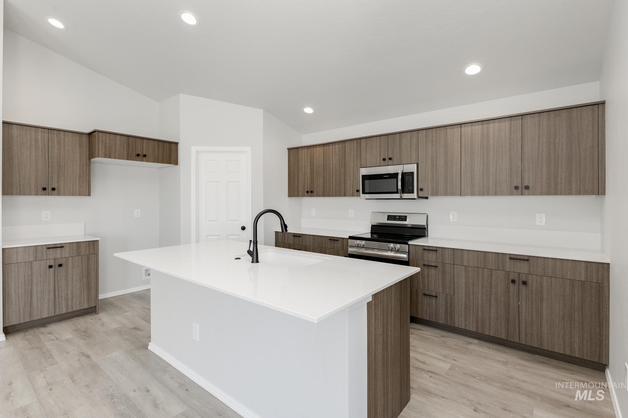 Kitchen with appliances with stainless steel finishes, light wood finished floors, brown cabinetry, and recessed lighting